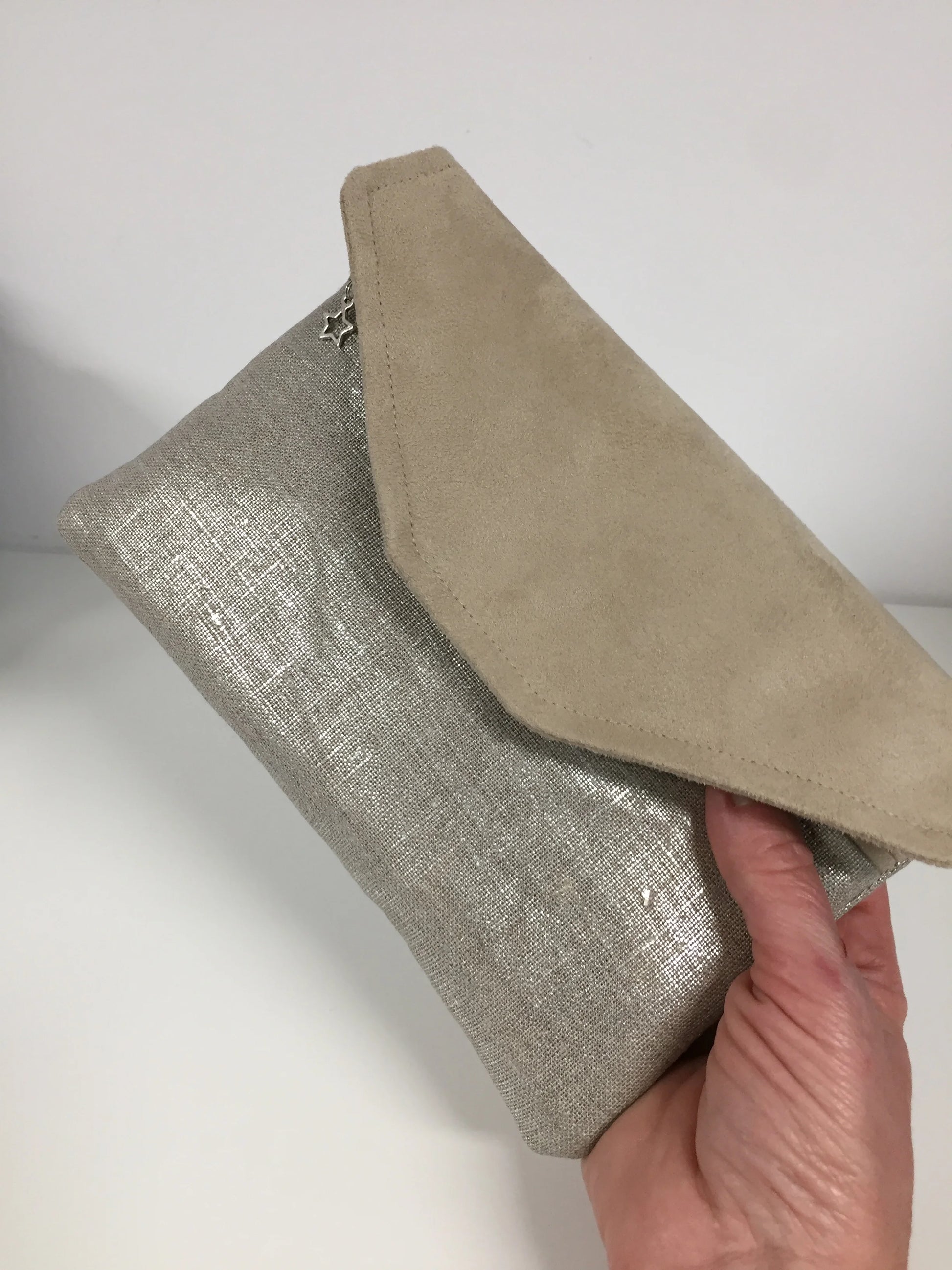 Le compagnon de sac beige en lin argenté, tenu en main.