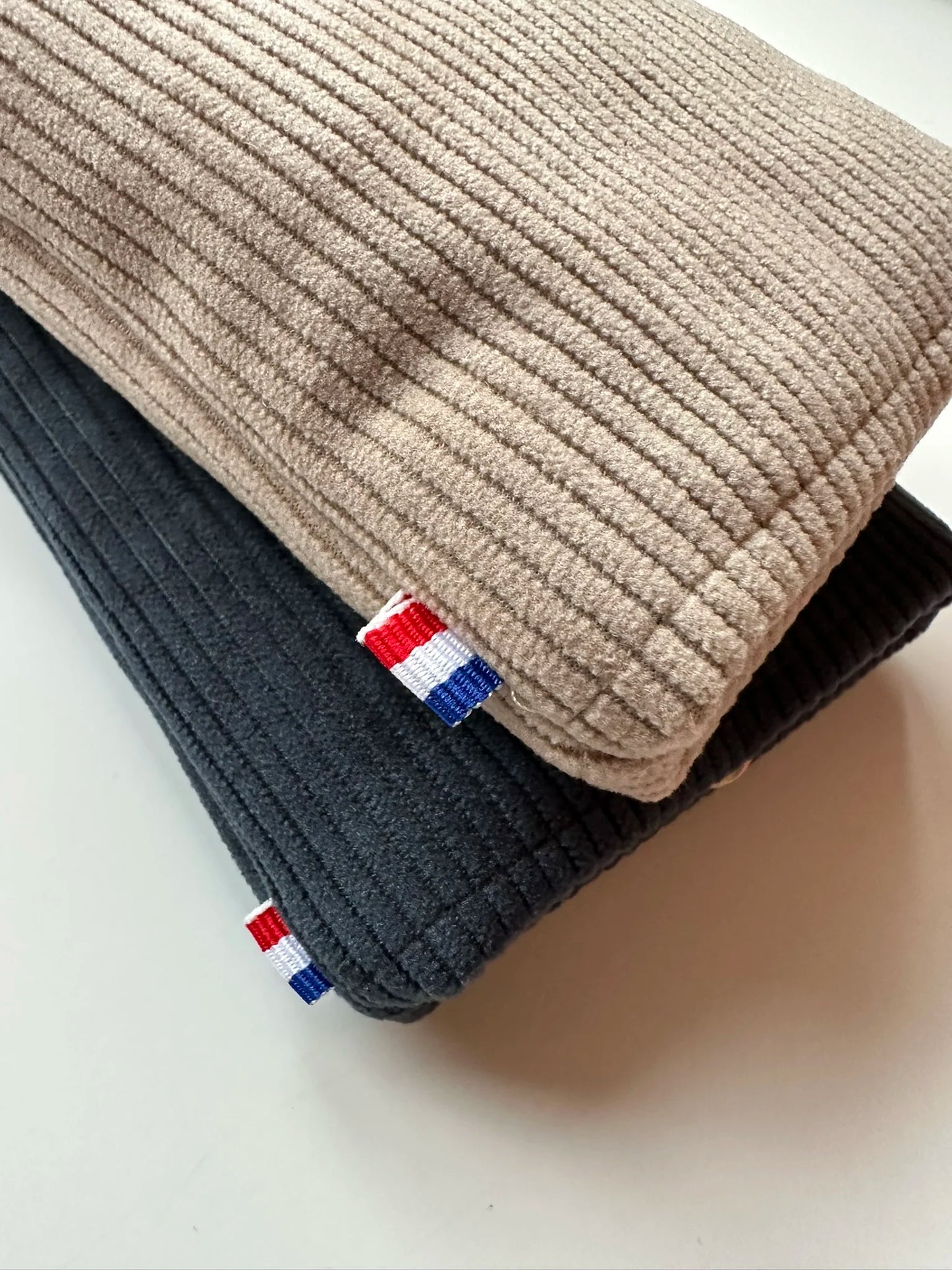 L'étui à lunettes en velours cotelé beige posé sur le bleu canard.