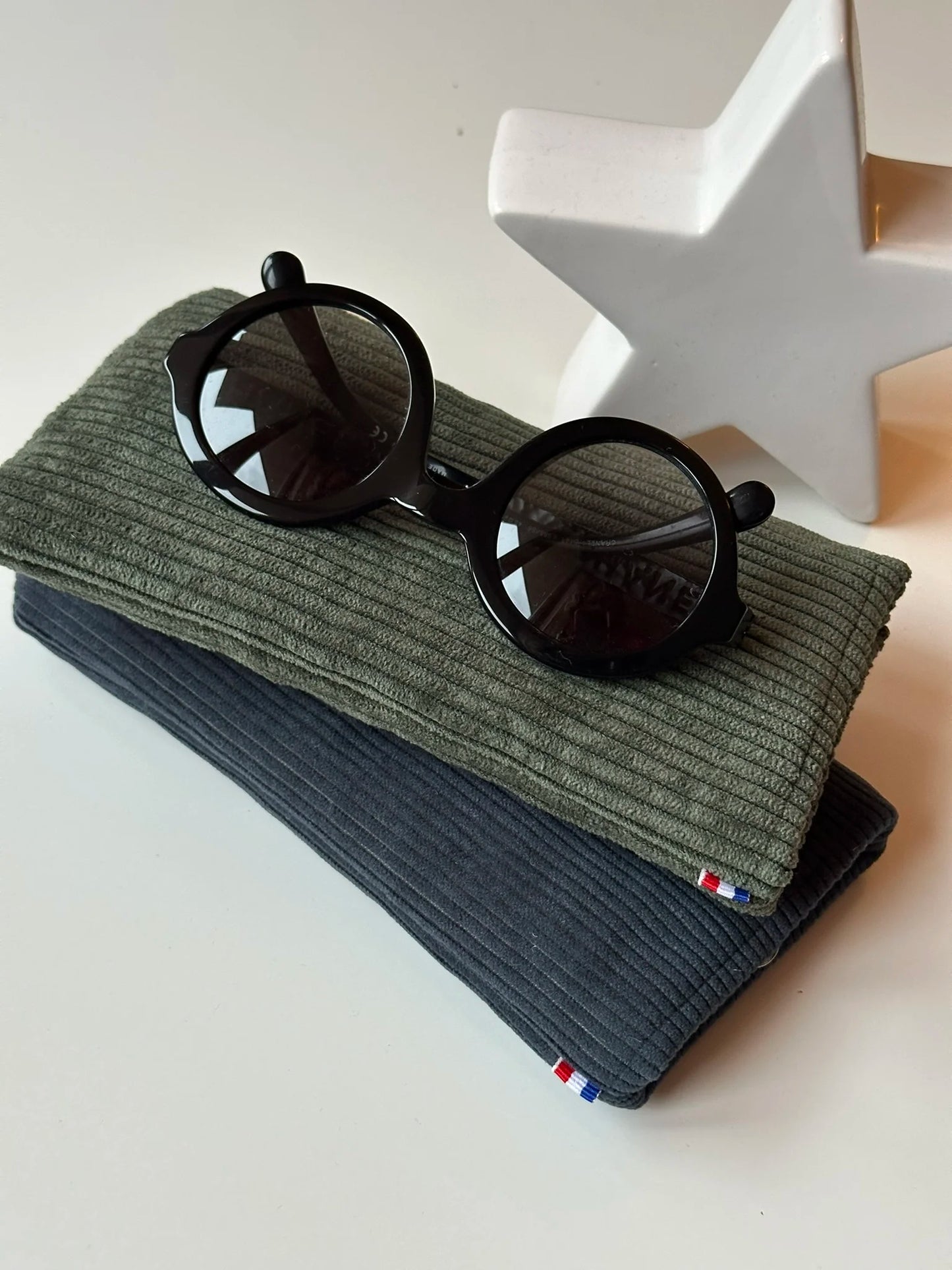 L'étui à lunettes en velours cotelé bleu canard sous le vert kaki.