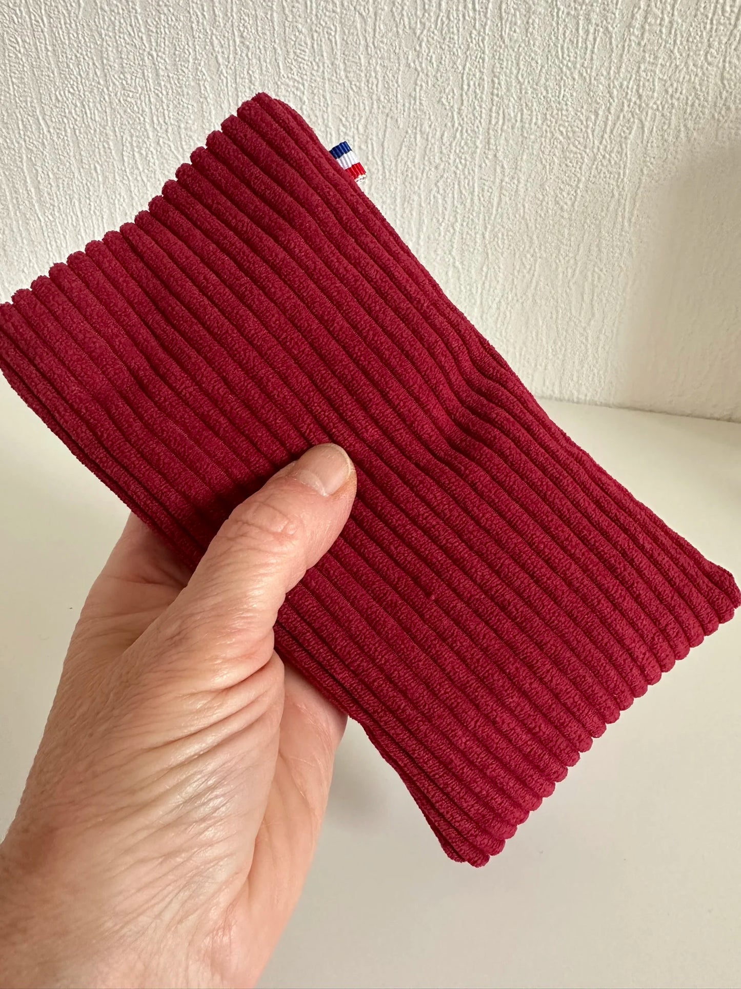 L'étui à lunettes en velours cotelé bordeaux tenu en main.