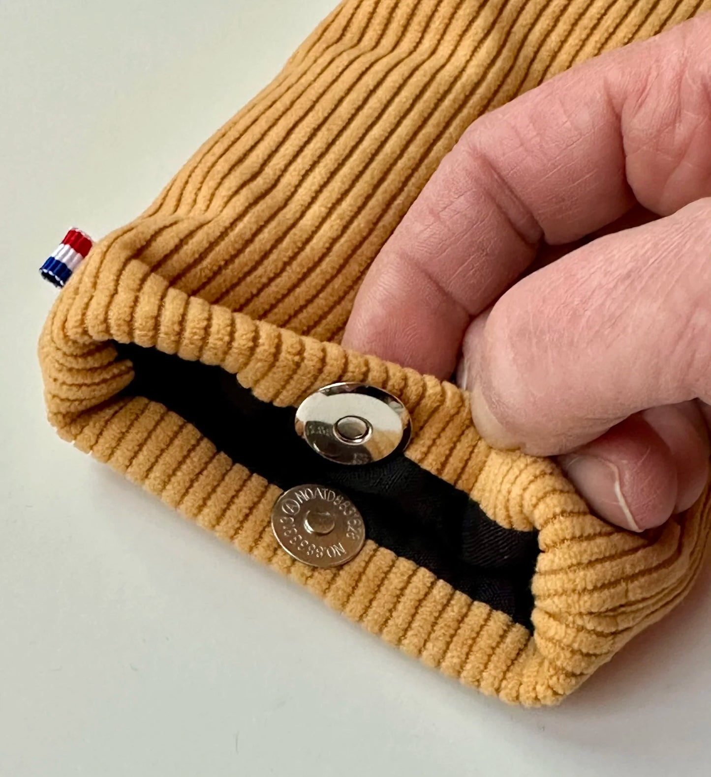 Le fermoir magnétique de l'étui à lunettes en velours cotelé jaune moutarde.