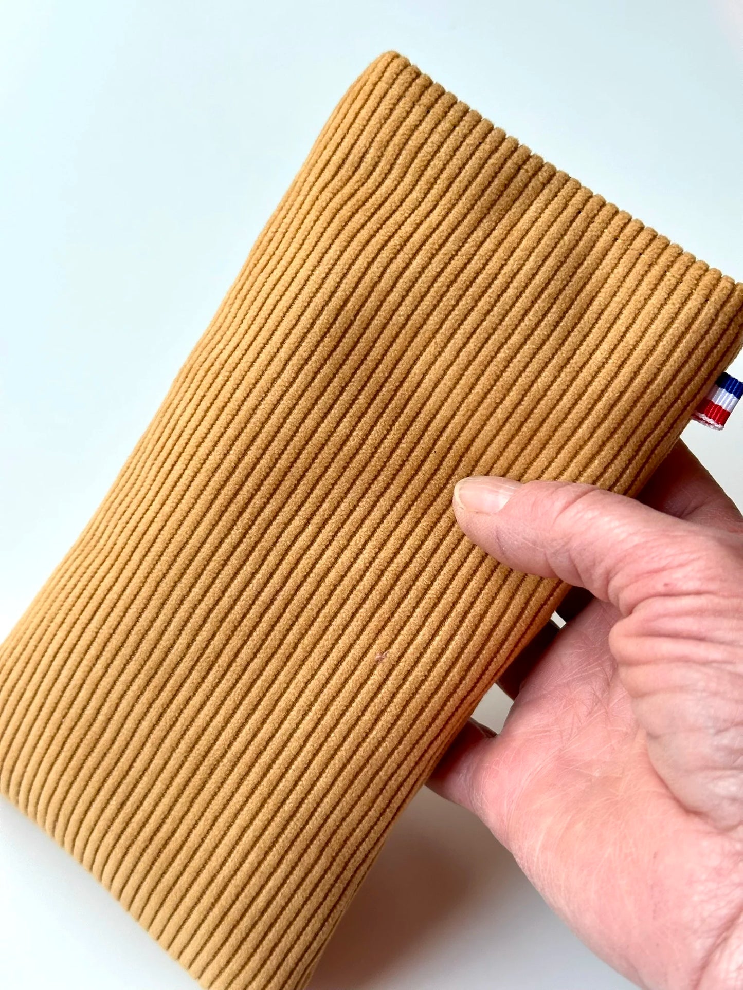 L'étui à lunettes en velours cotelé jaune moutarde, dans la main.