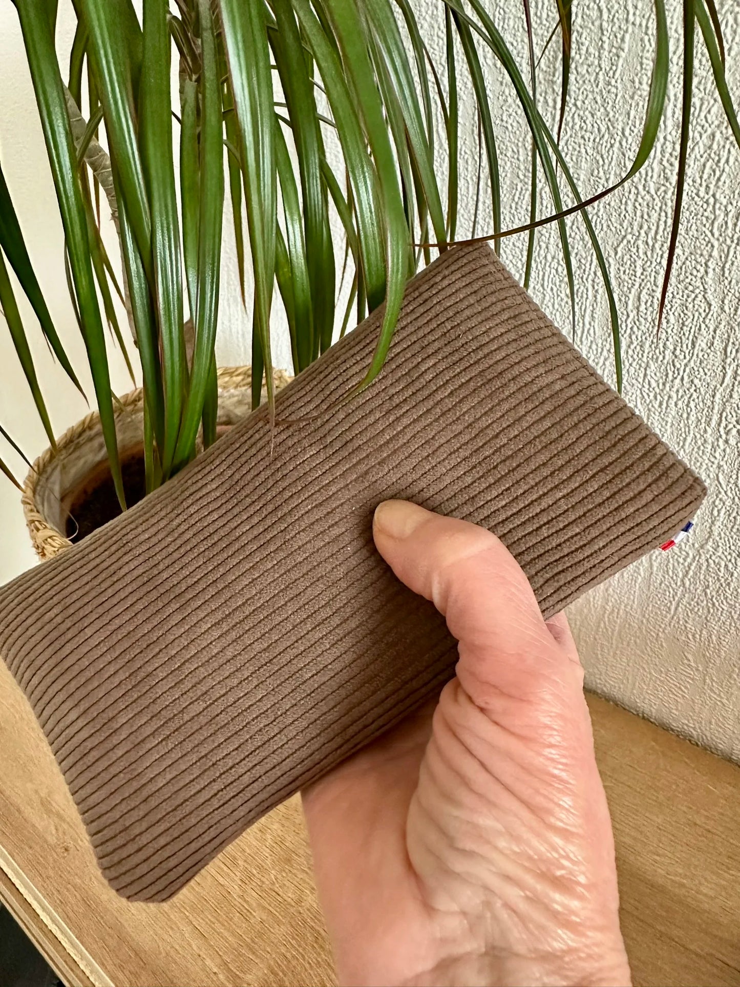 L'étui à lunettes en velours cotelé marron chamois, tenu en main.