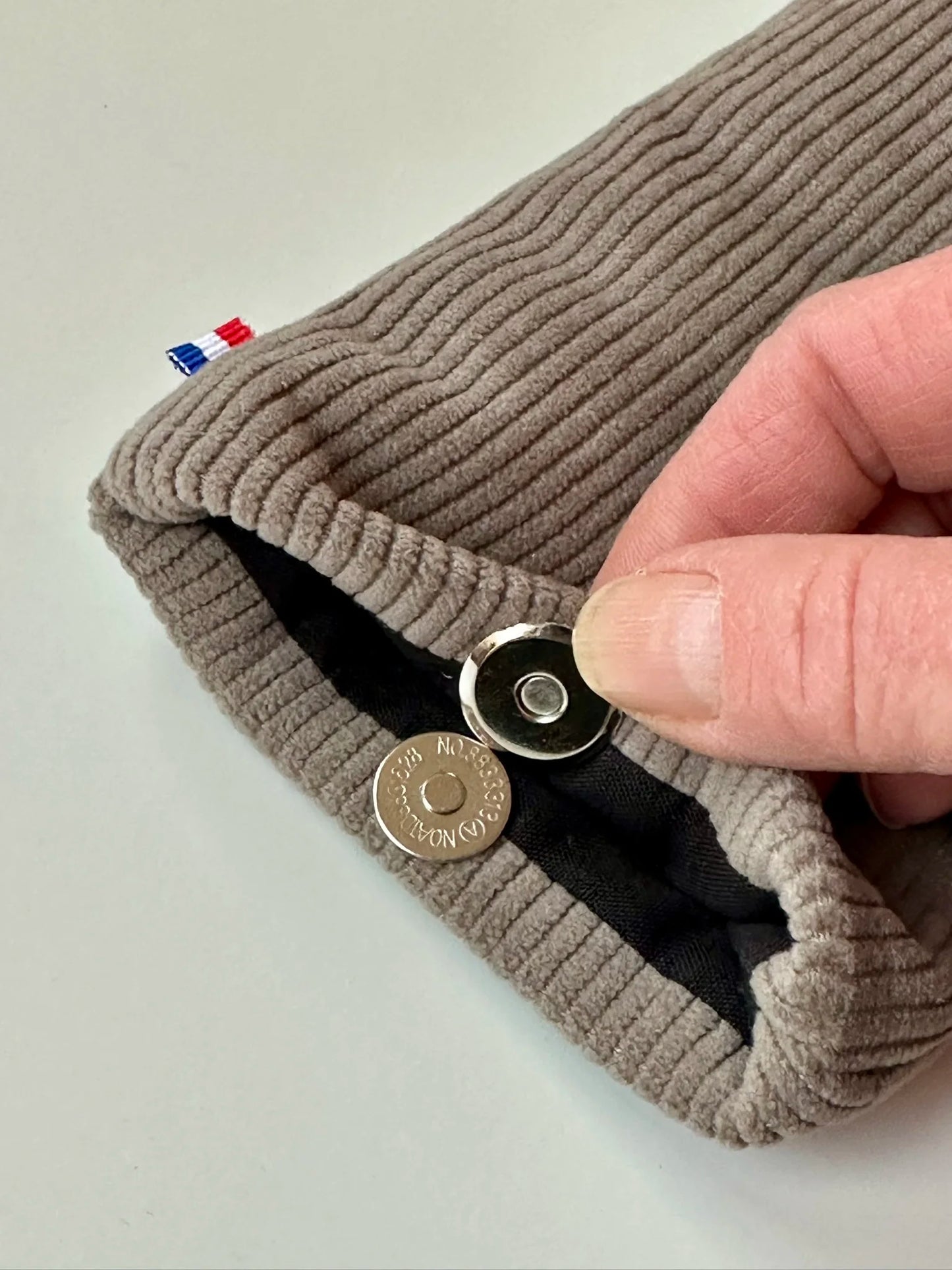 Le fermoir magnétique de l'étui à lunettes en velours cotelé taupe.