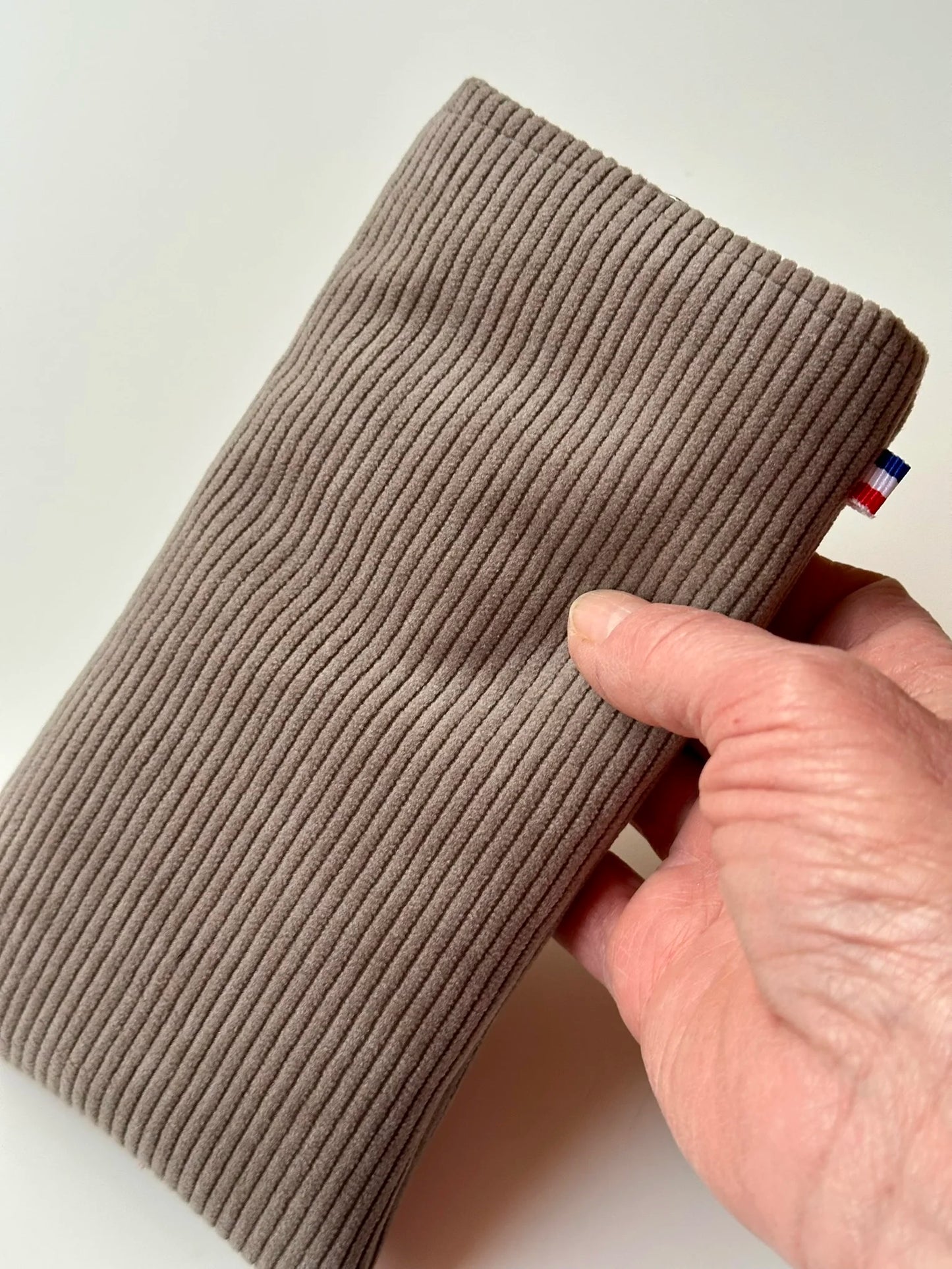 L'étui à lunettes en velours cotelé taupe, tenu en main.