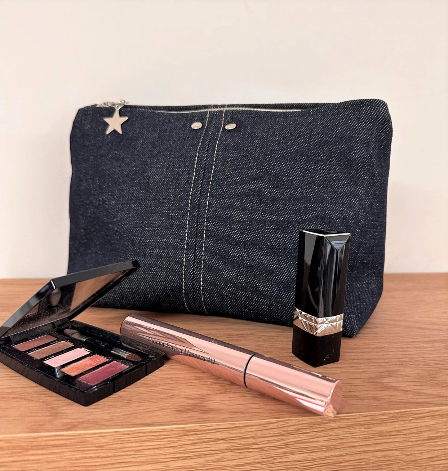 La pochette en denim brut, fermée, présentée avec maquillage.