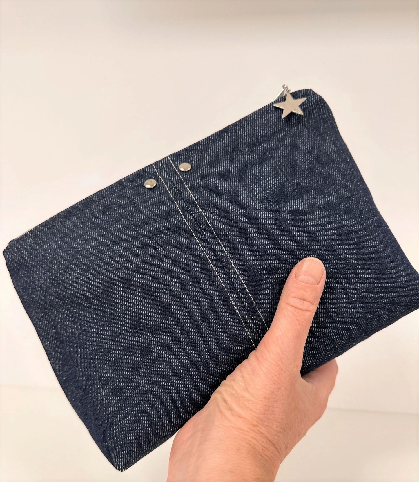 La pochette en denim brut, portée à la main.
