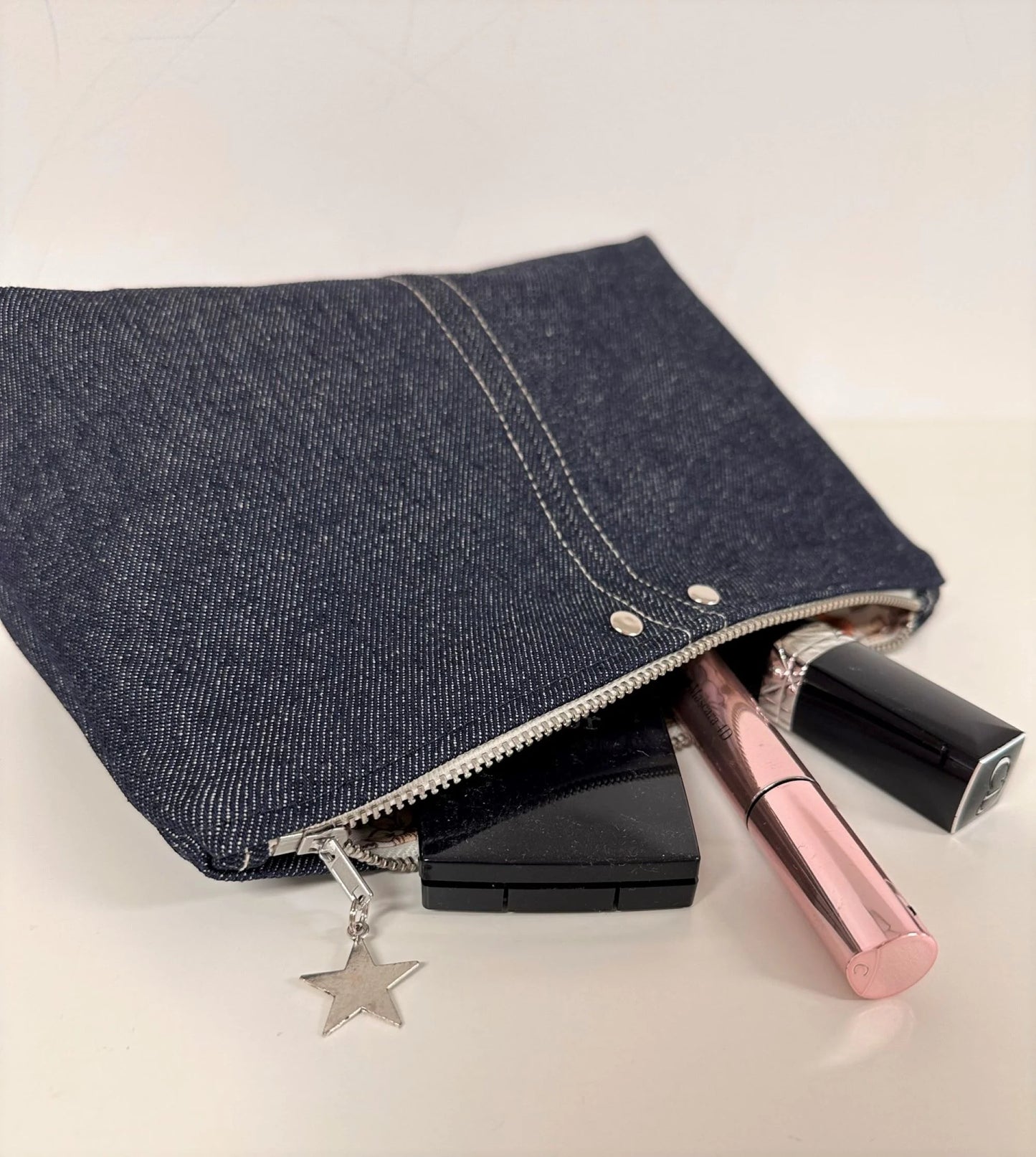 La pochette à maquillage en denim brut, avec ses rivets et surpiqures.