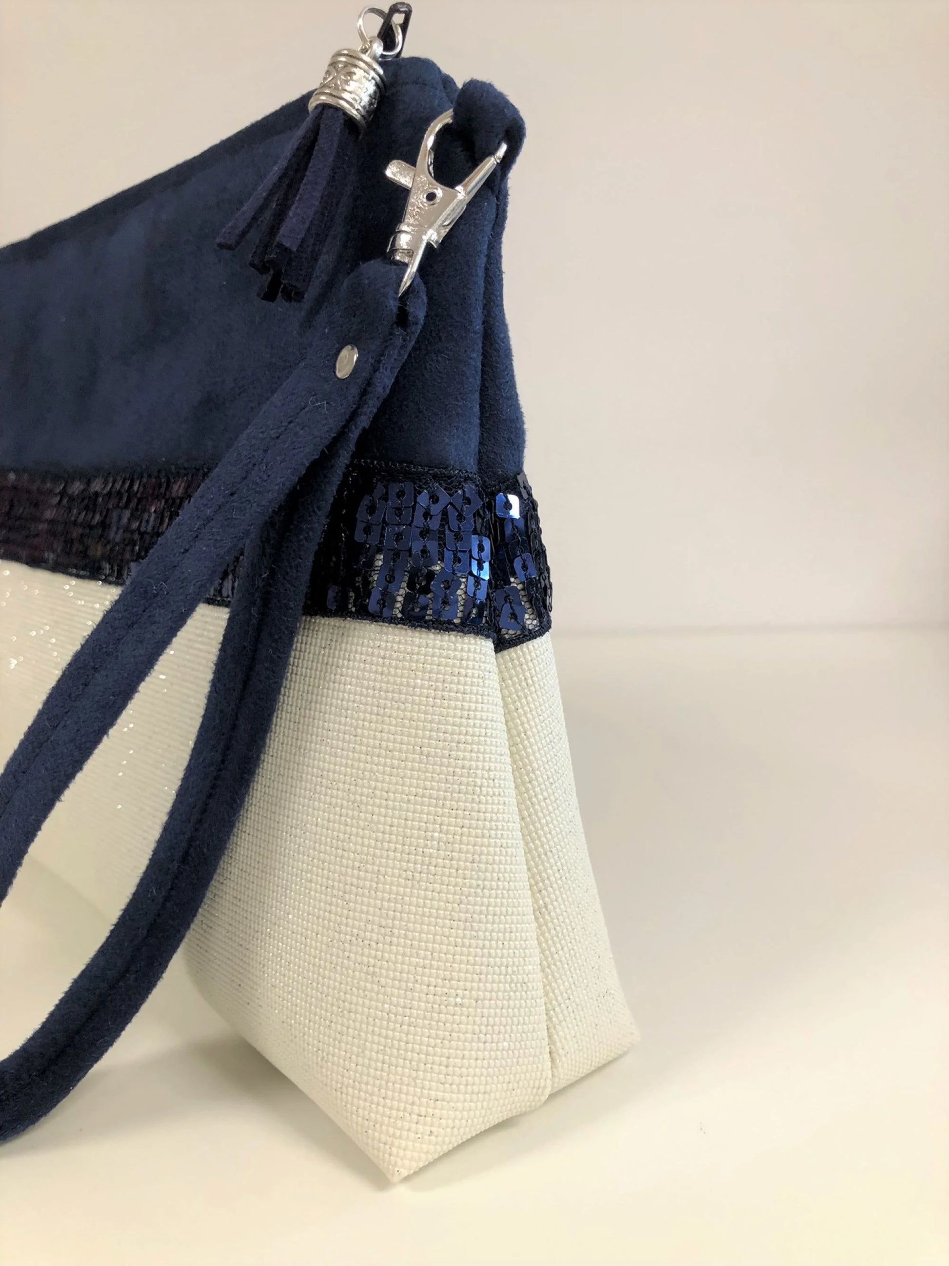 Vue détaillée de la pochette Isa zippée bleu marine et blanc à paillettes avec sa dragonne amovible.