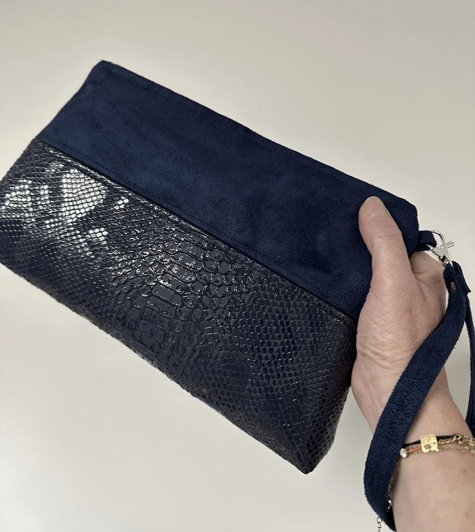 La pochette Isa zippée bleu marine aspect reptile, tenue en main.