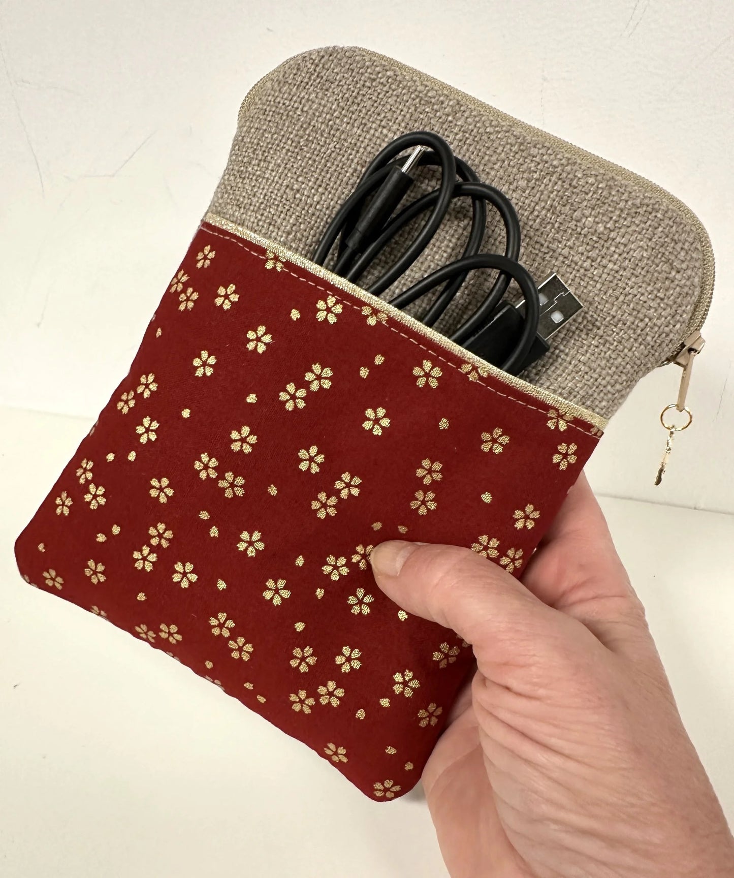 La pochette liseuse en lin et tissu japonais rouge à fleurs dorées, tenue en main.