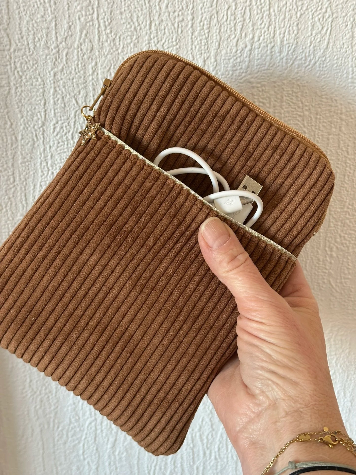 La pochette liseuse en velours cotelé caramel tenue à la main.