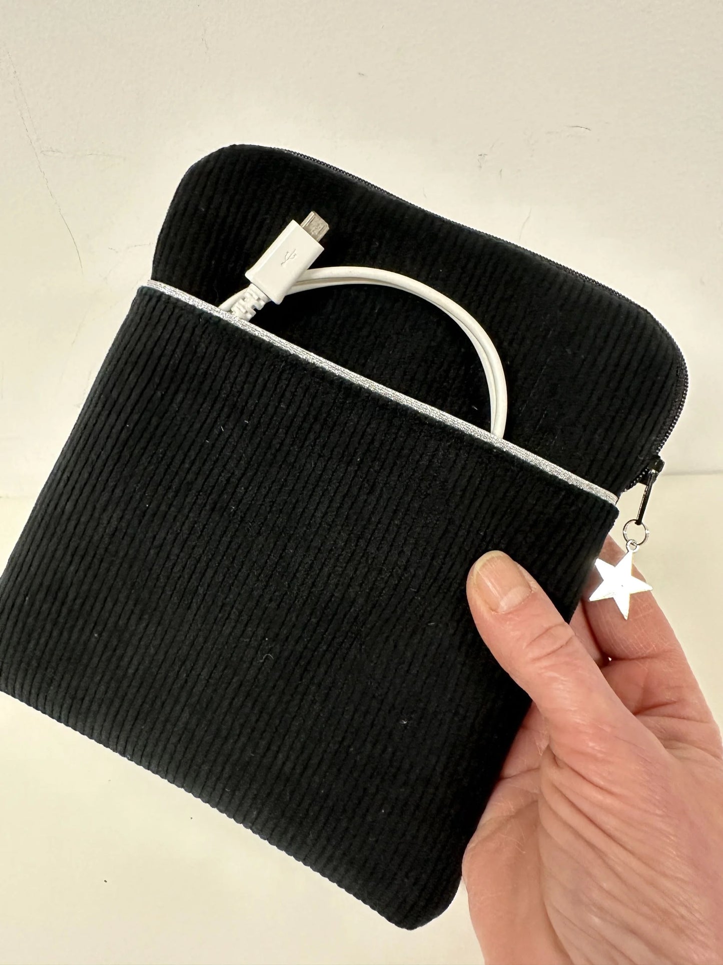 La pochette liseuse en velours cotelé noir, tenue en main.