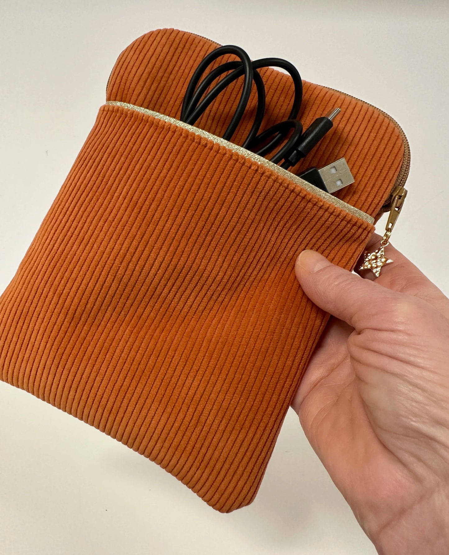 La pochette liseuse en velours cotelé orange tenue en main.