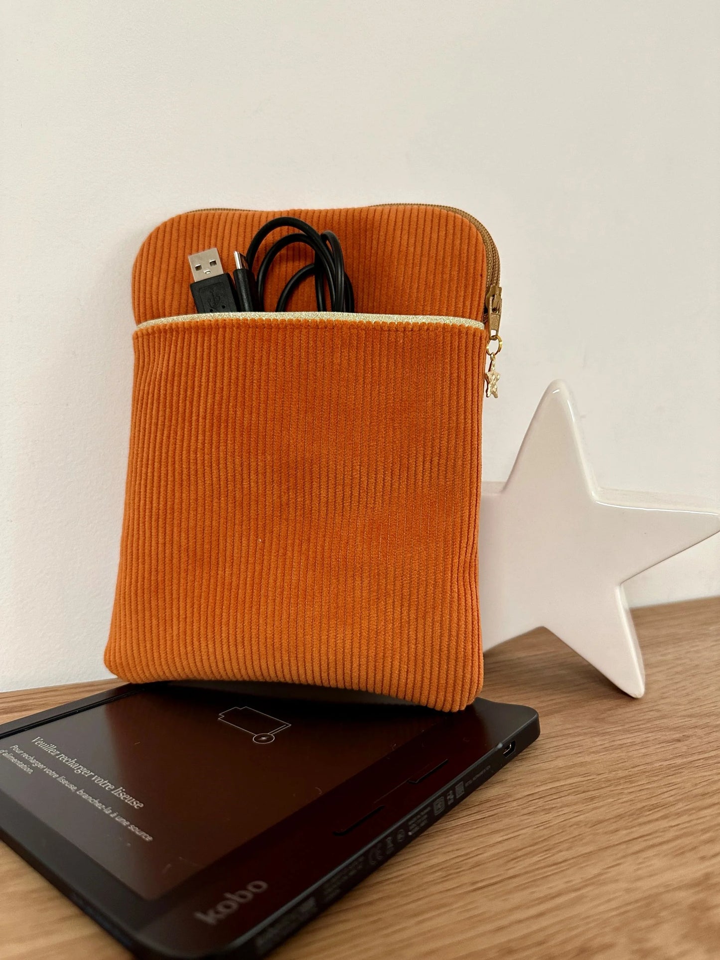 La pochette liseuse en velours cotelé orange, avec câble dans la poche avant.