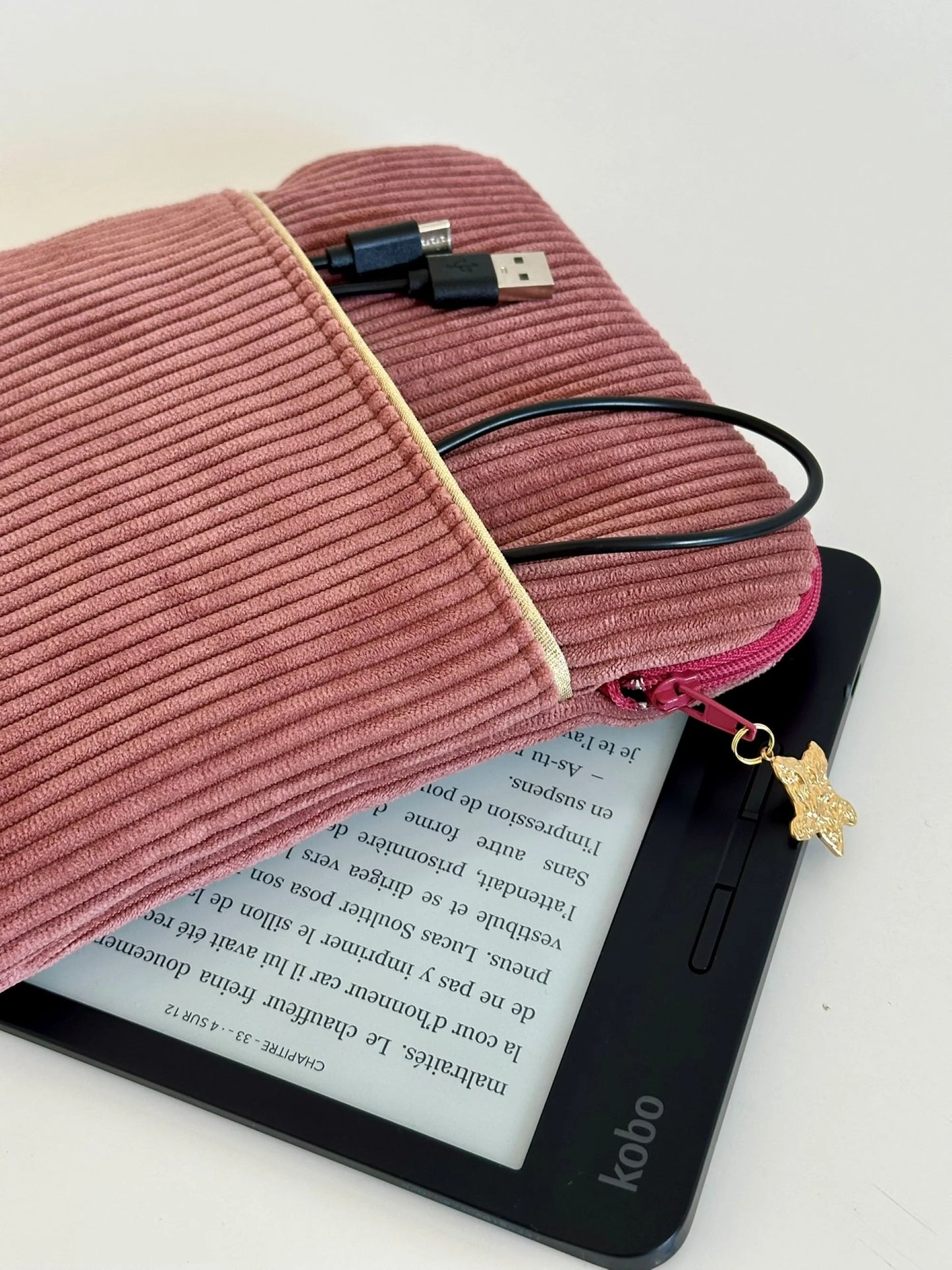 Le cable de chargement dans la poche avant de la pochette liseuse en velours cotelé vieux rose.