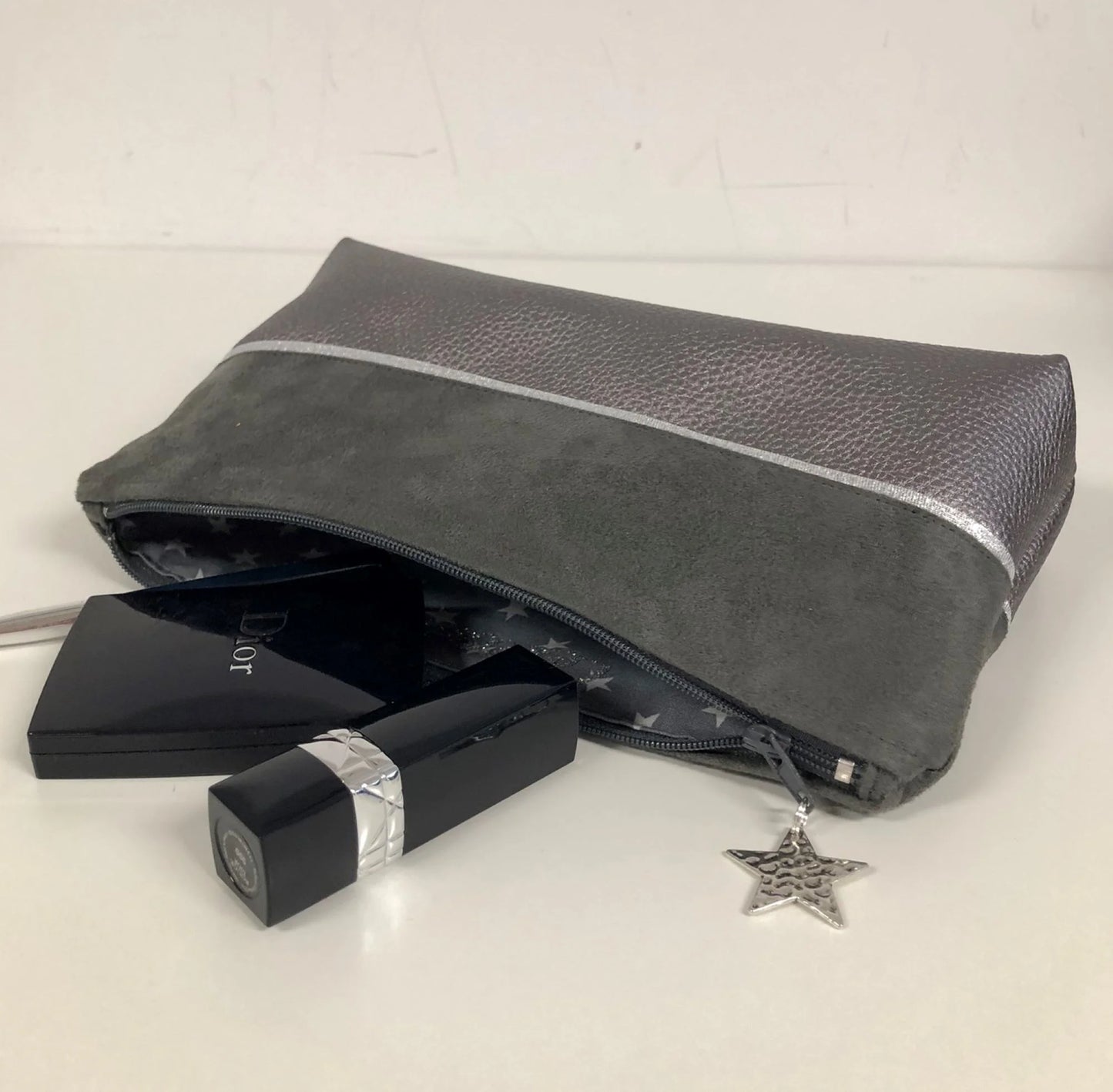 pochette à maquillage grise et argentée, entrouverte.