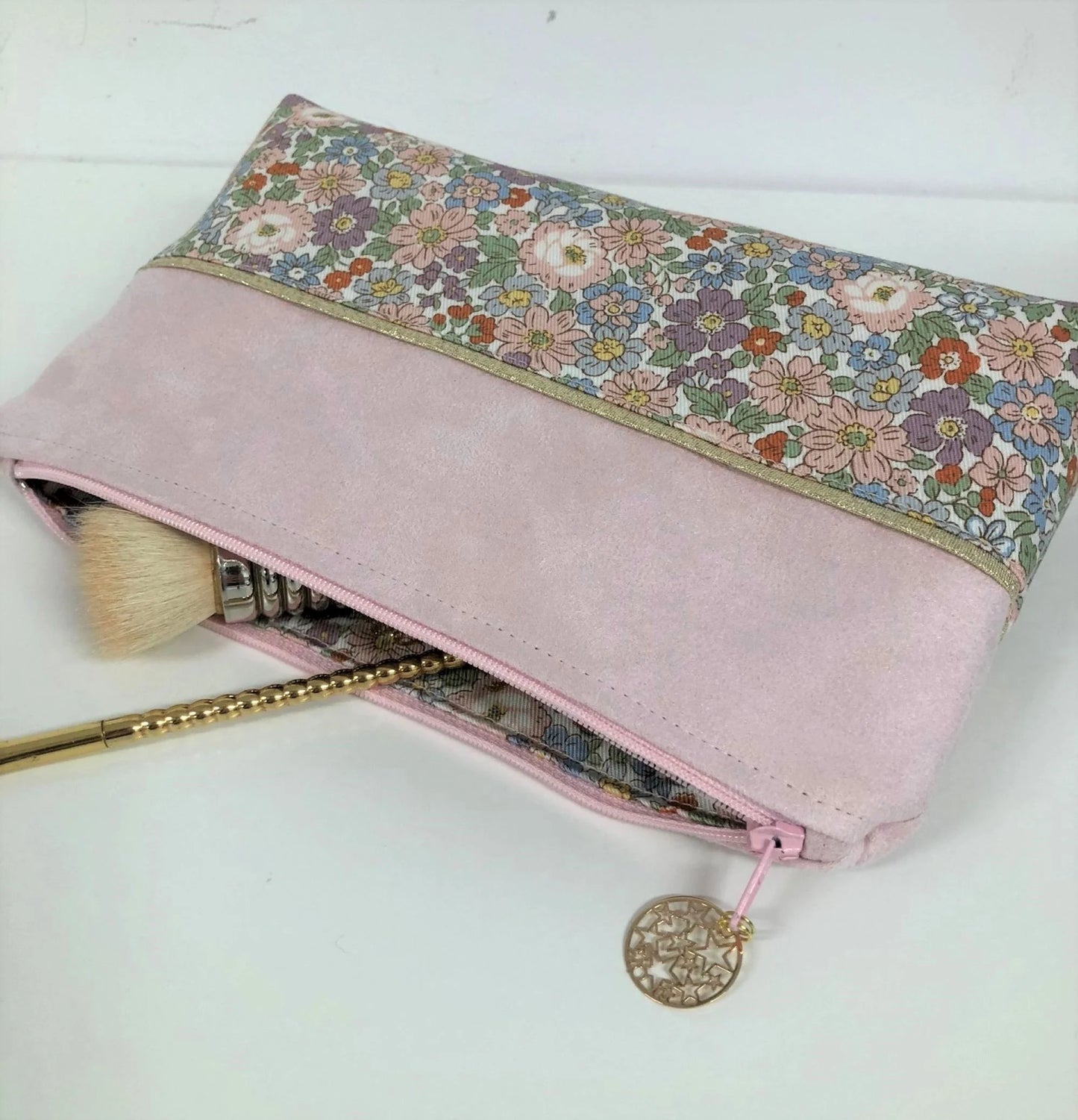 La pochette à maquillage rose et dorée à fleurs pastel, entrouverte.