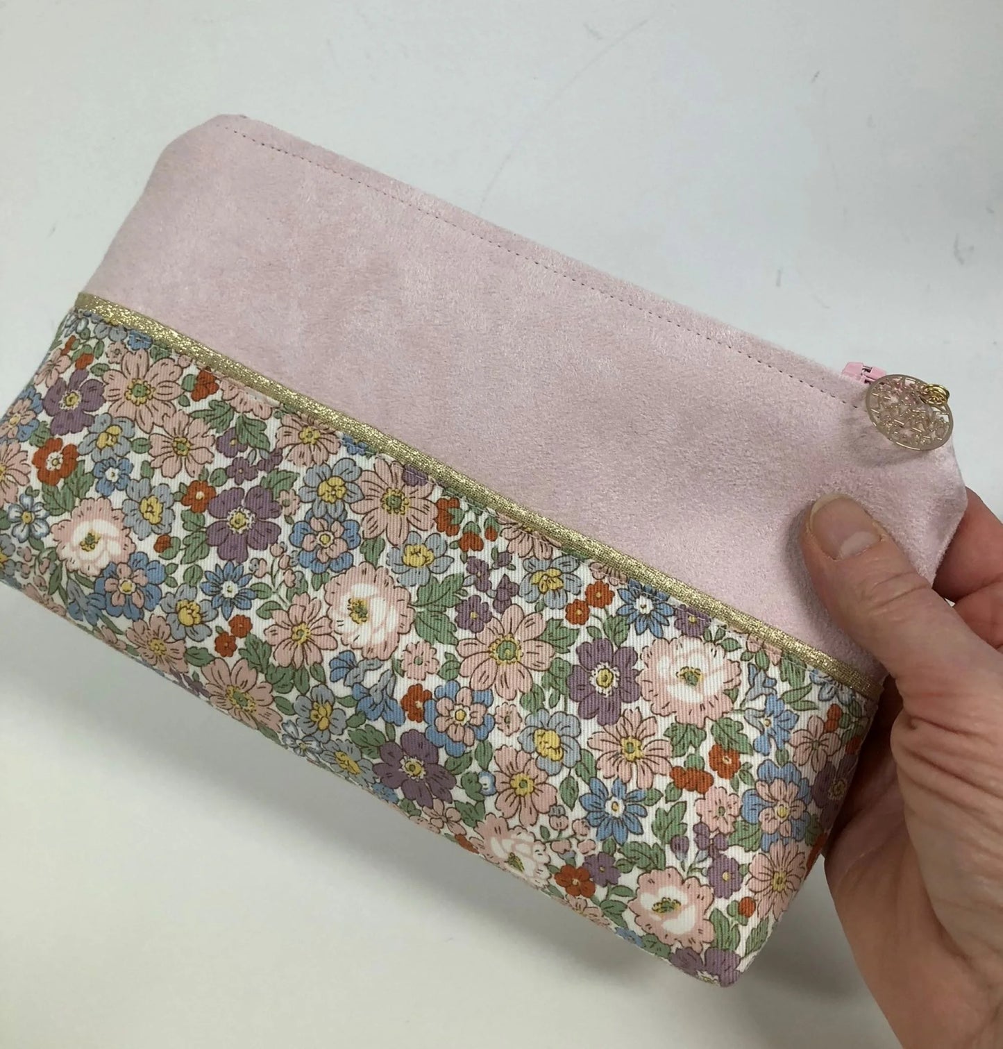 La pochette à maquillage rose et dorée à fleurs pastel, tenue en main.