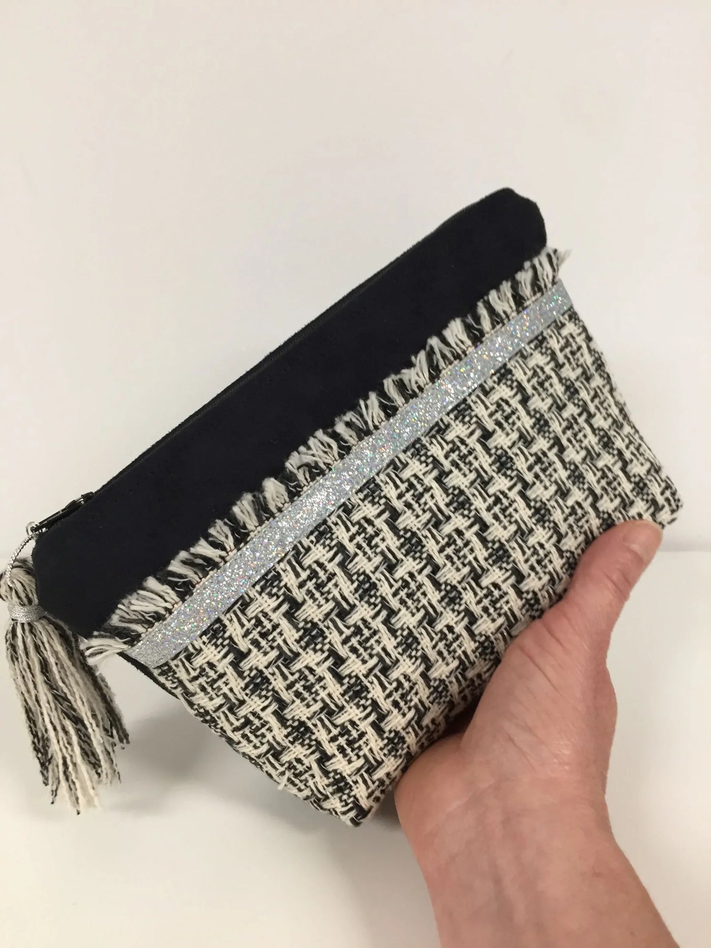 La pochette noire et écru en tweed style haute couture française, tenue dans la main.