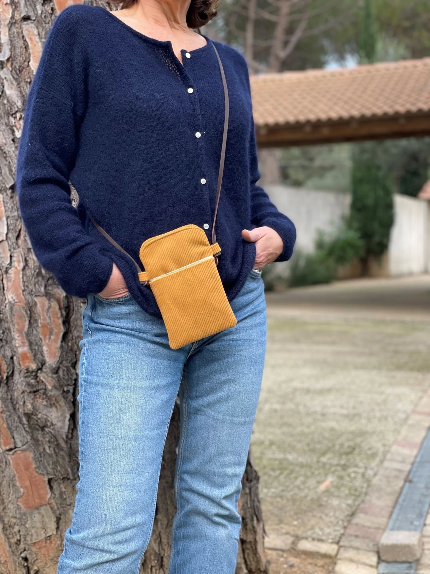 La pochette telephone bandoulière en velours cotelé jaune moutarde et cuir marron, portée en travers.