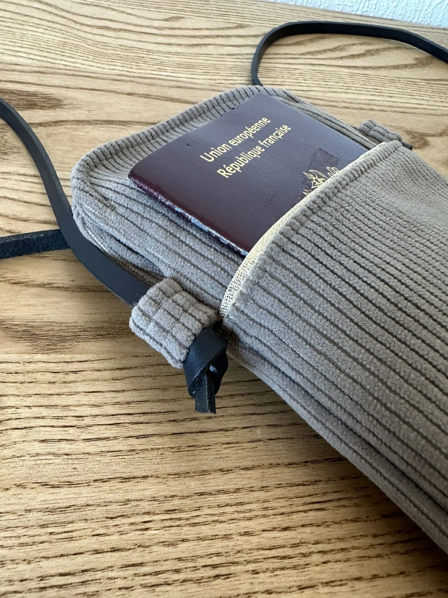 La lanière en cuir noir nouée de la pochette téléphone en velours cotelé taupe .