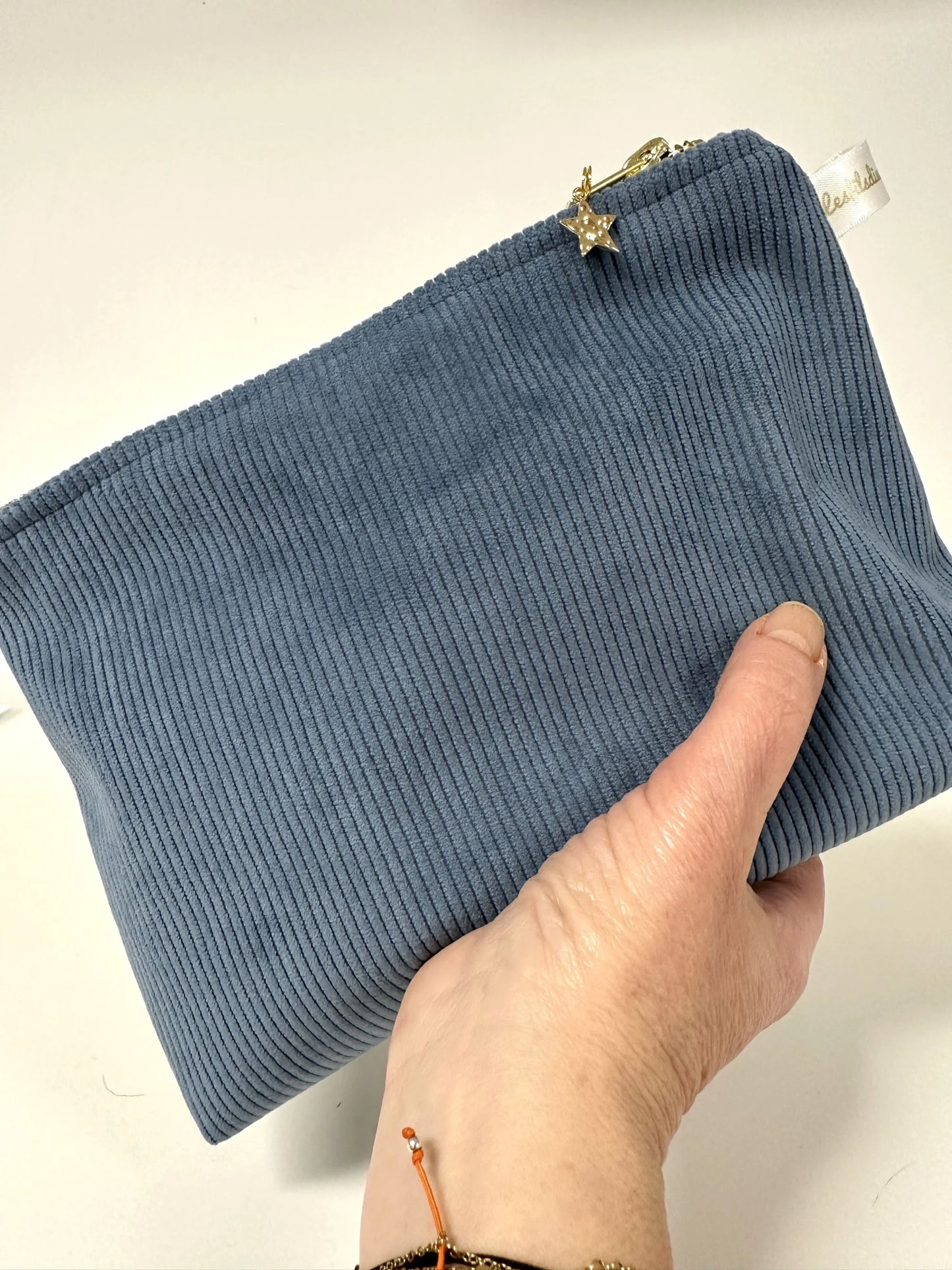 La pochette en velours côtelé bleu azur, tenue en main.