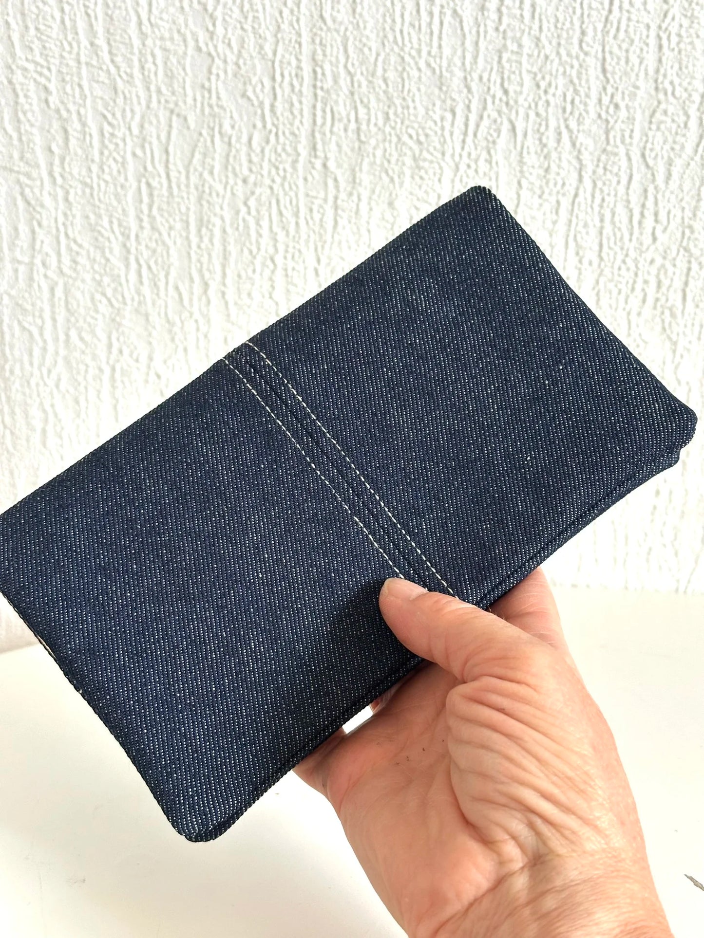 Le porte chéquier en denim tenu en main.