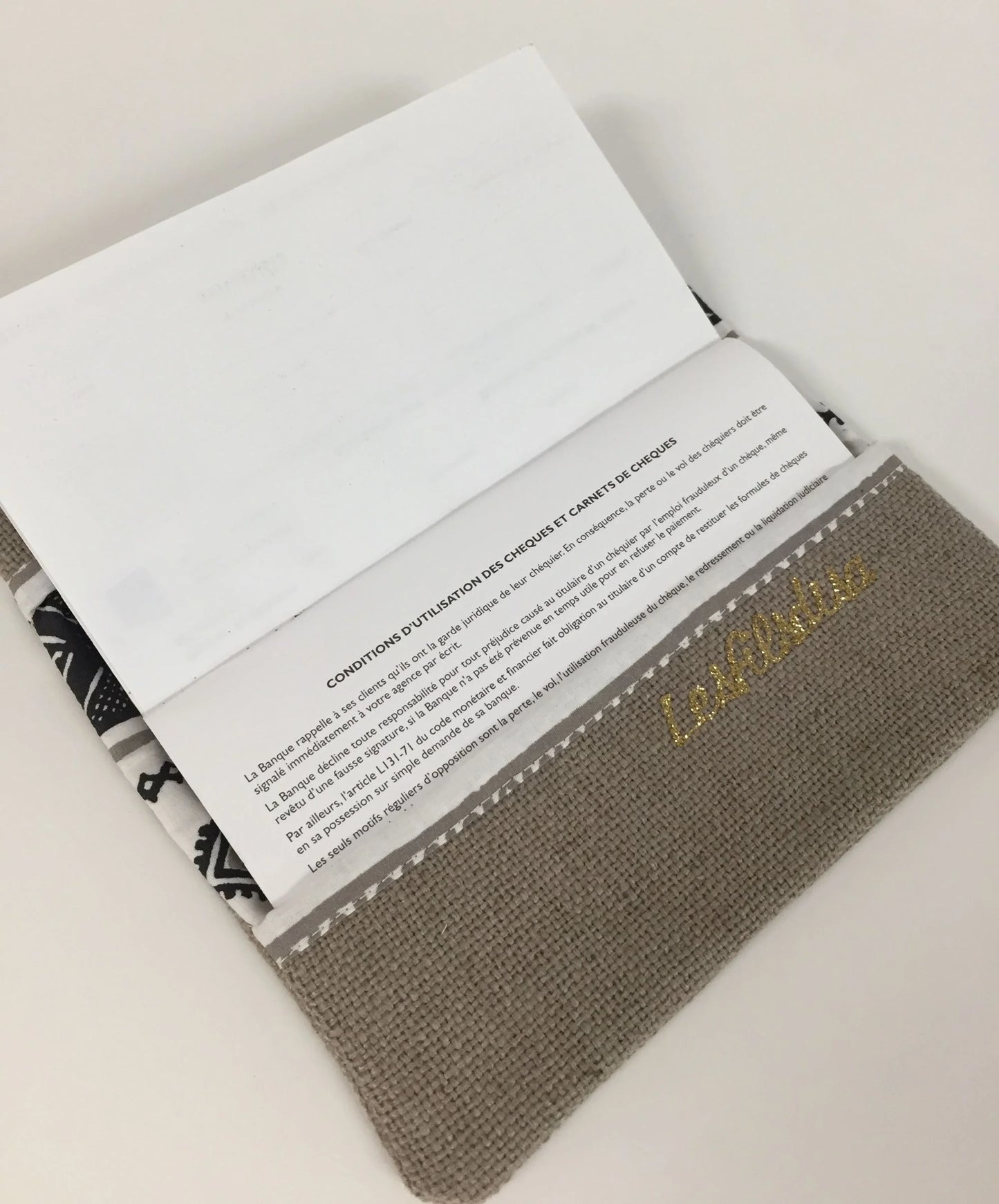 Le rabat inférieur du porte-chéquier ethnique beige, blanc et doré.