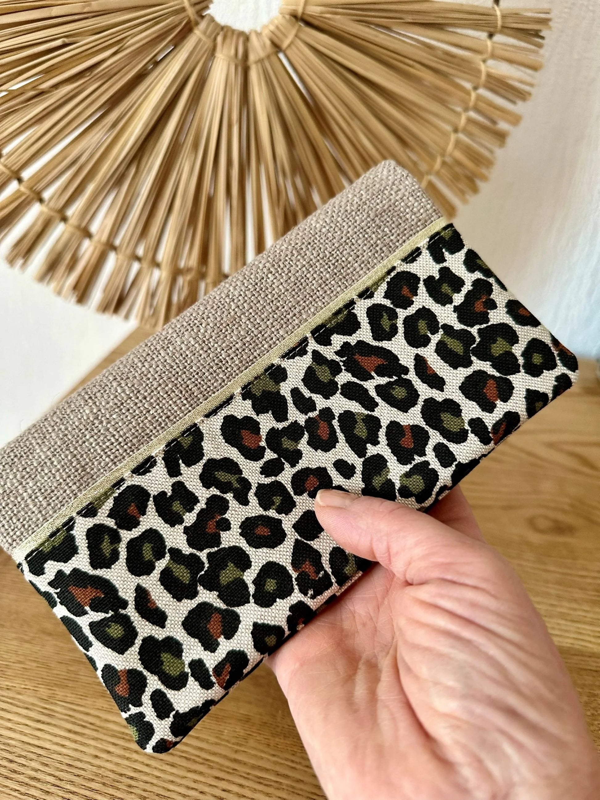 Le porte chéquier léopard en lin beige, tenu en main.