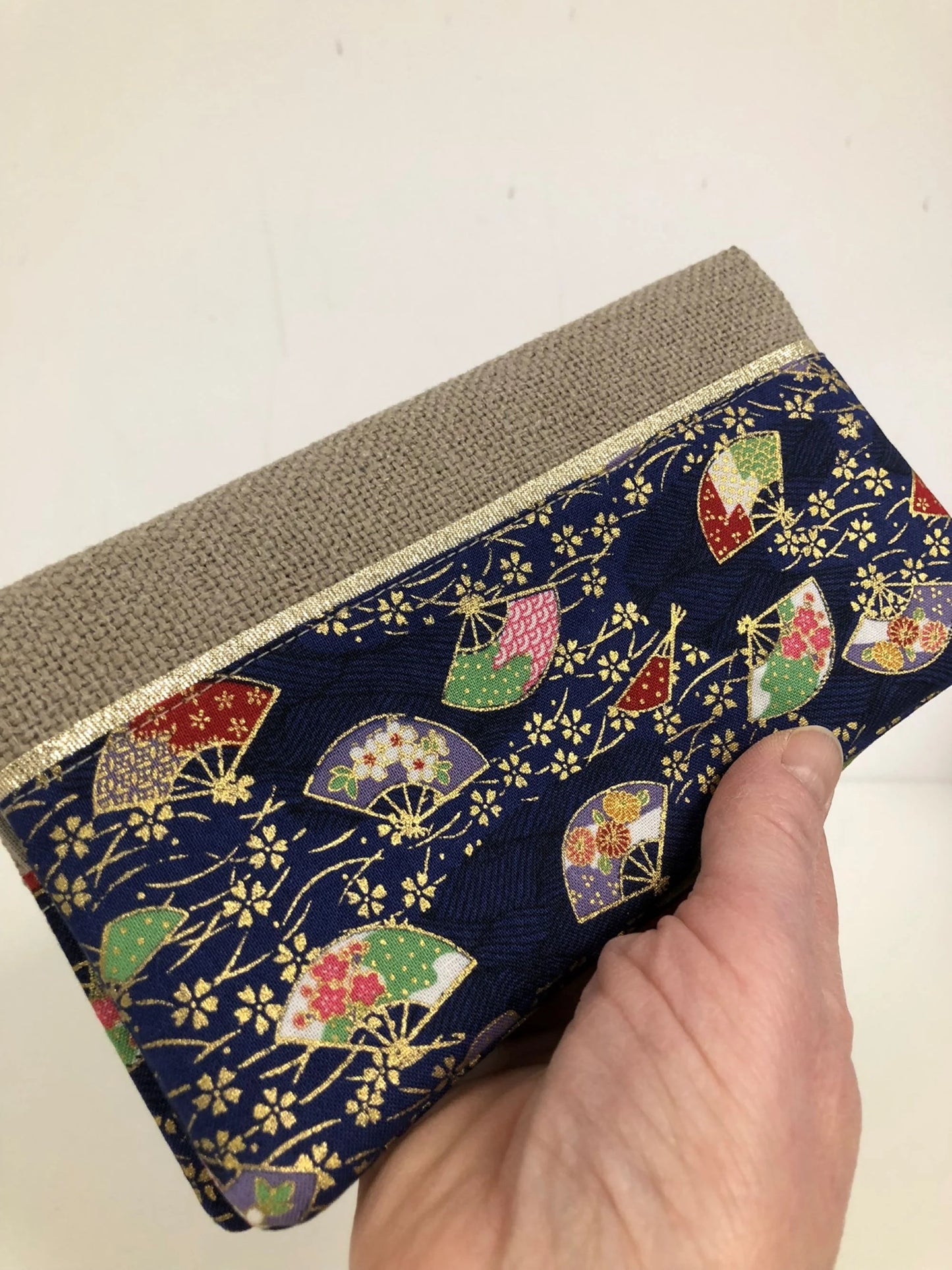 Le porte-chéquier en lin beige et tissu japonais bleu éventails, tenu en main.