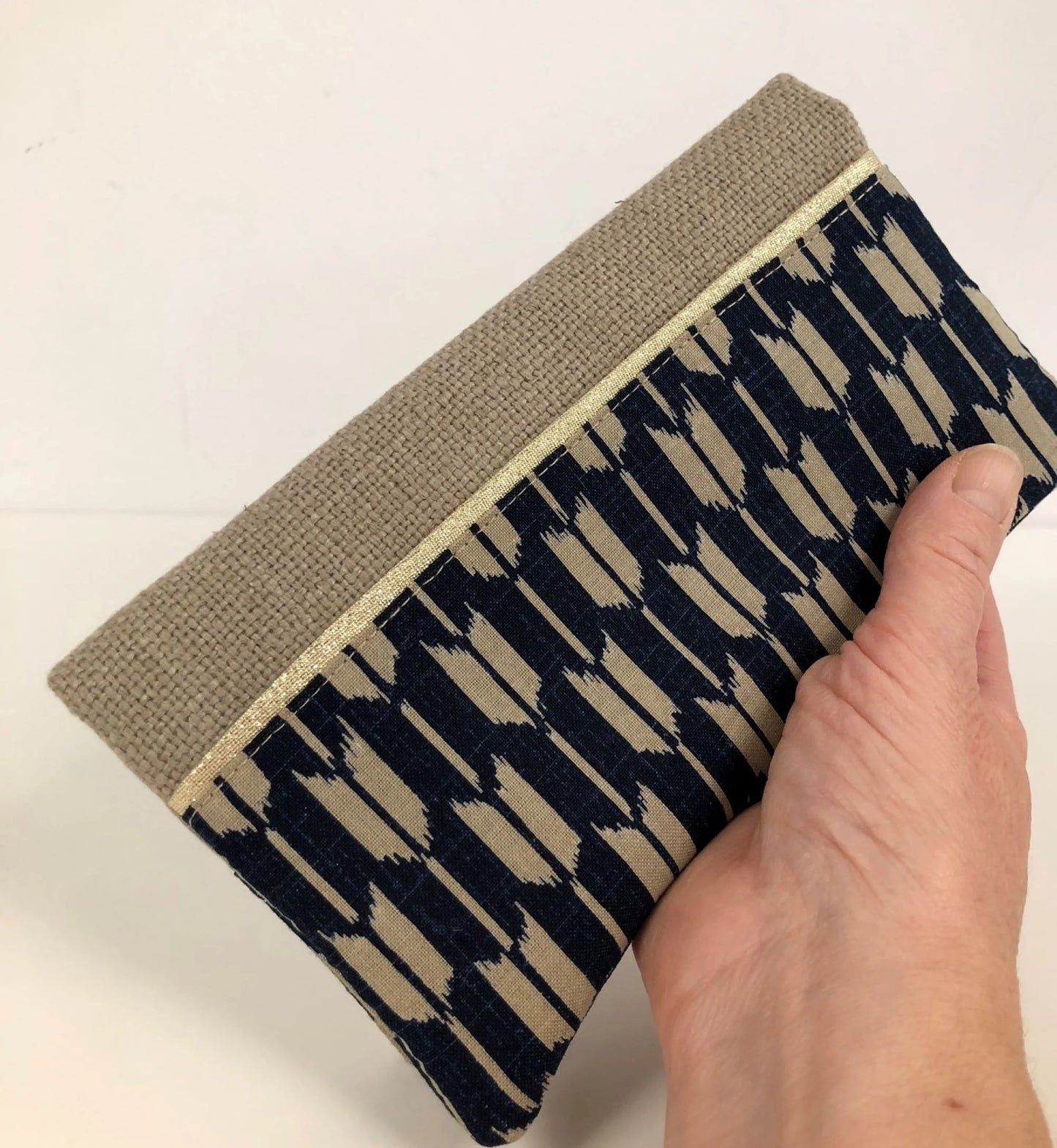 Le porte chéquier en lin beige et tissu japonais fléchés yabanes, tenu en main.