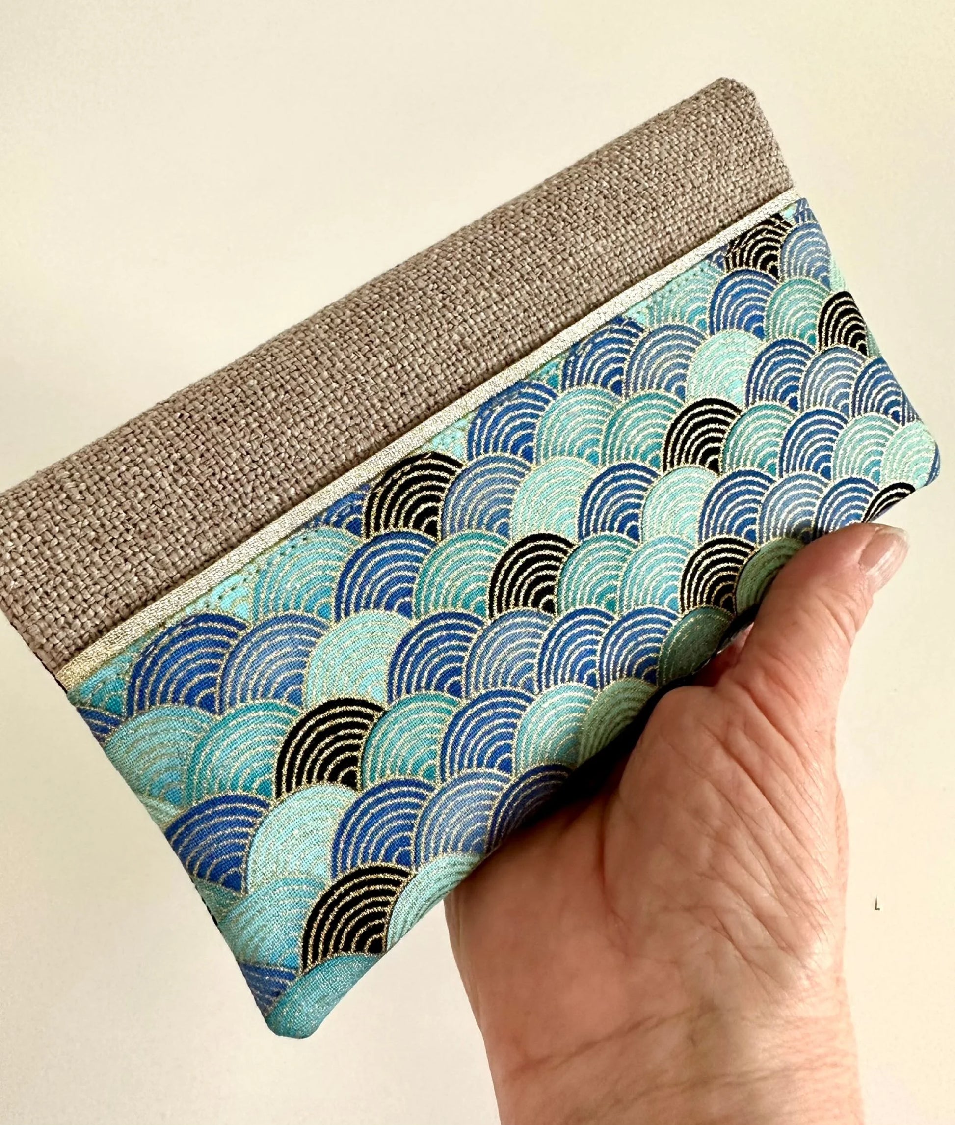Le porte chéquier en lin et tissu japonais bleu turquoise, tenu en main.