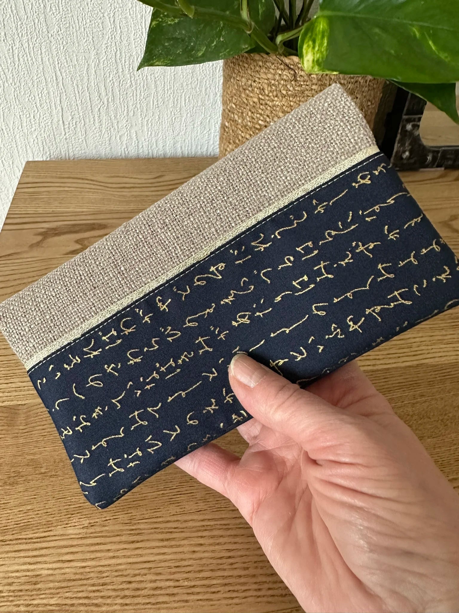 Le porte chéquier en lin et tissu japonais écriture dorée, tenu en main.