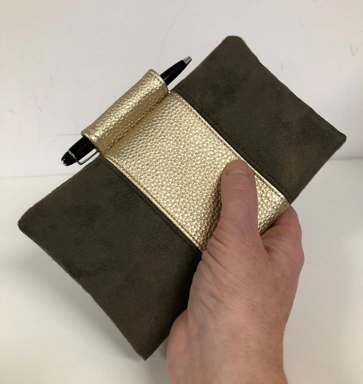 Le porte-chéquier marron et doré avec porte-stylo, porté en main.