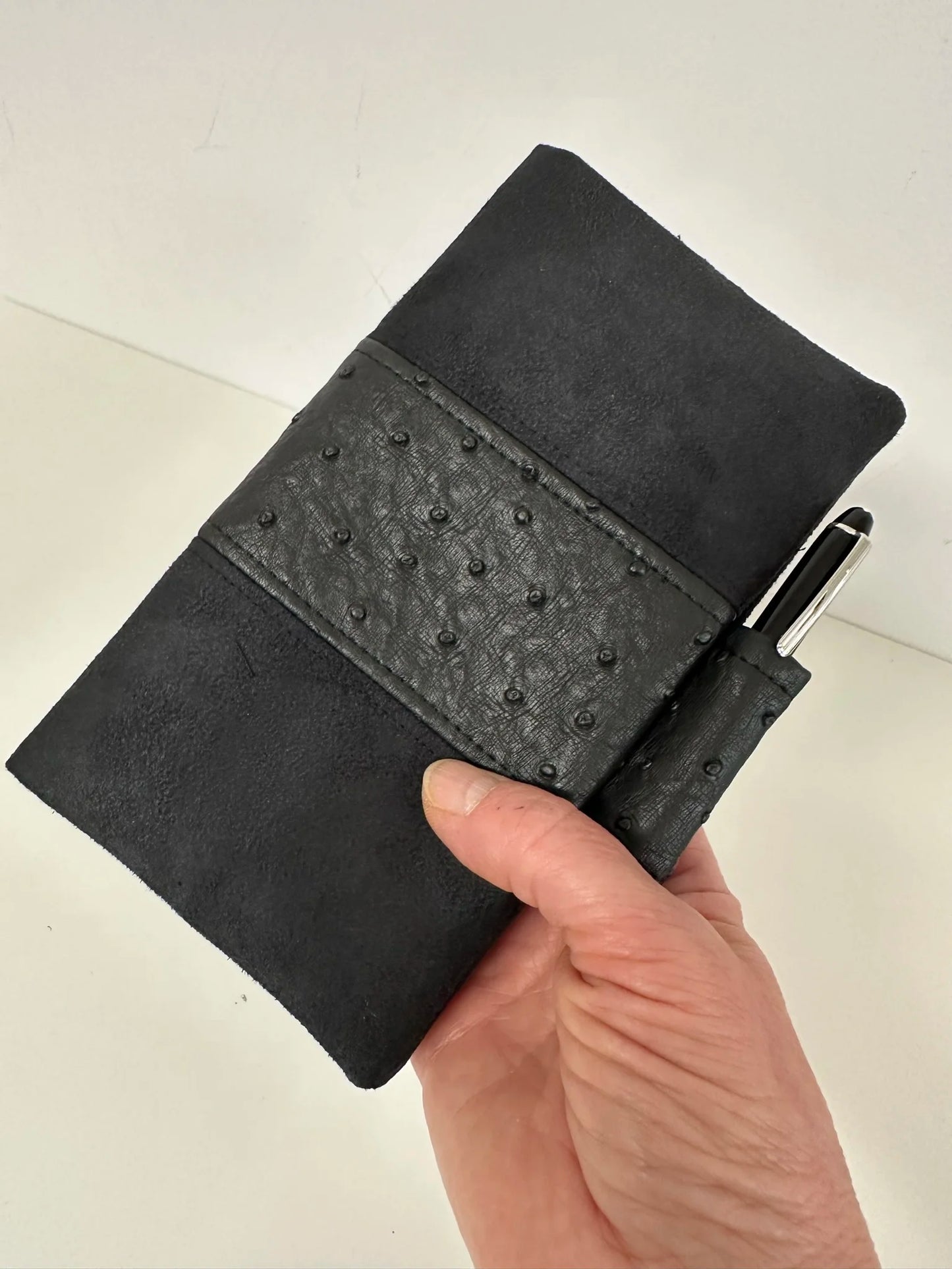 Le porte chéquier noir mat exotique avec porte stylo, tenu en main.