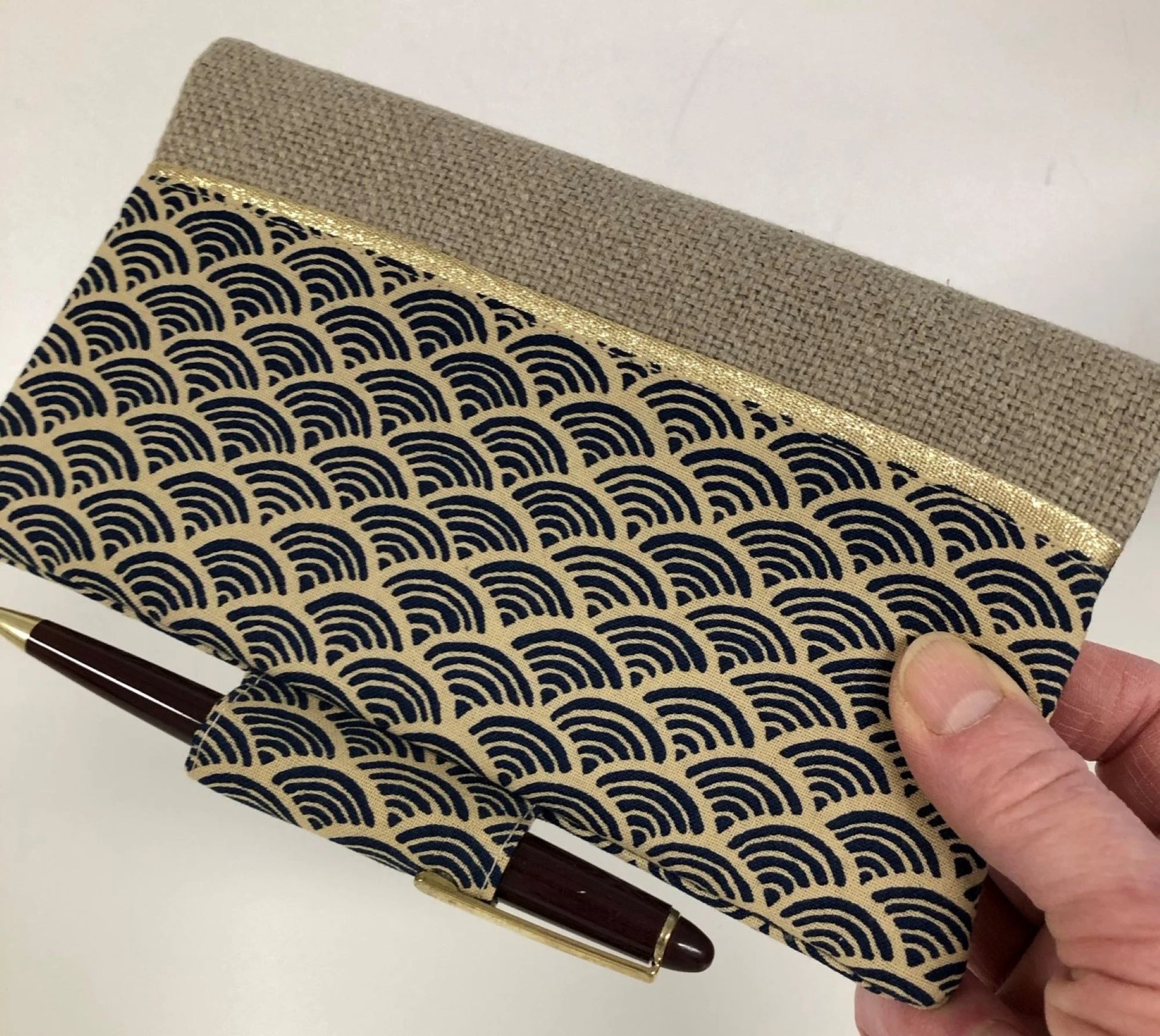 Le porte-chéquier avec porte stylo en lin et tissu japonais Seigaiha, tenu en main.