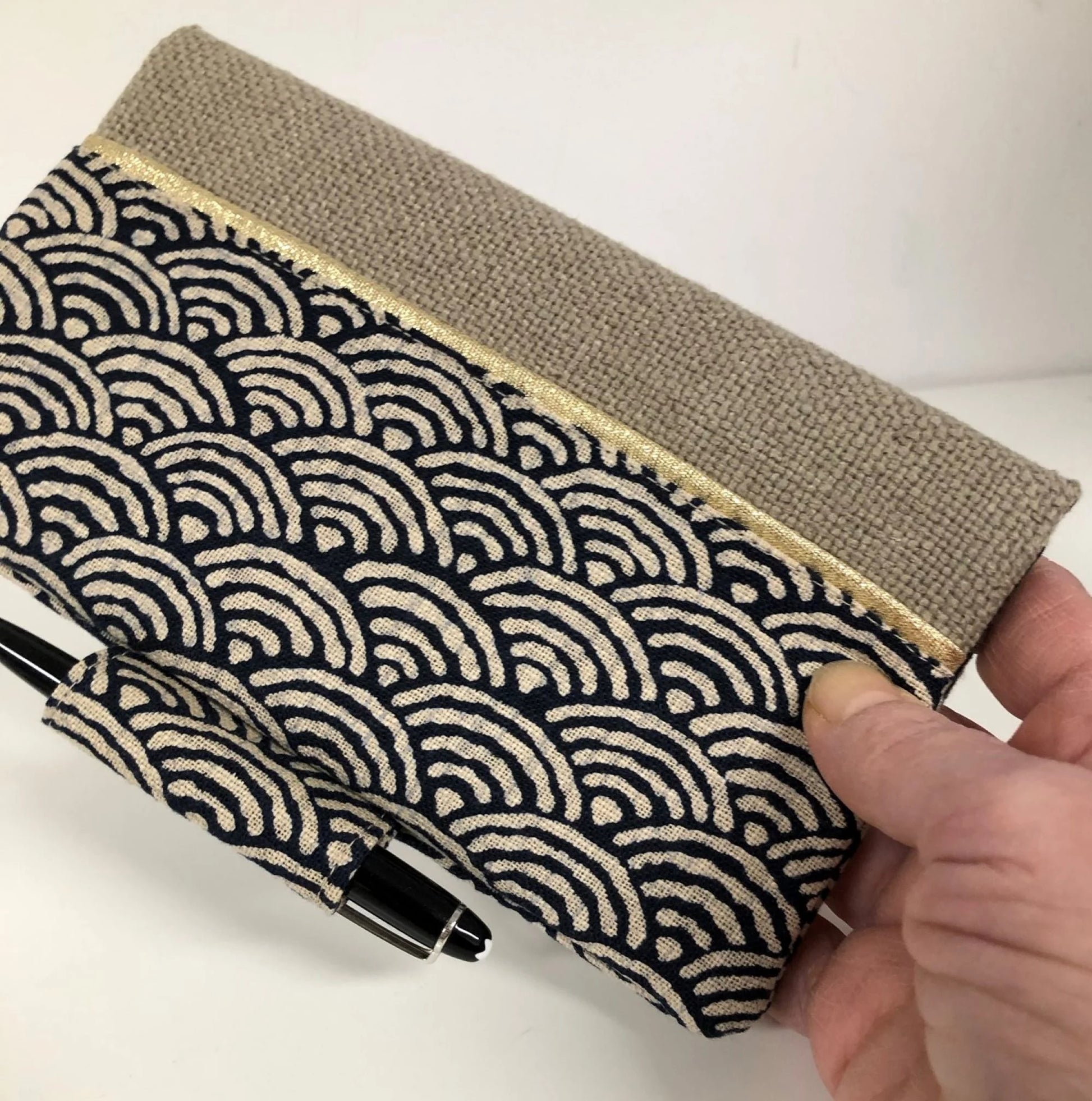 Le porte chéquier avec porte stylo en lin et tissu japonais Seigaiha bleu nuit, tenu en main.
