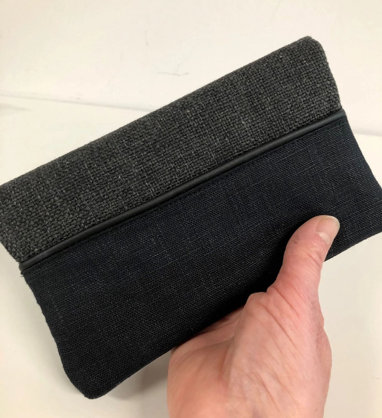 Le porte-chéquier unisexe en lin gris anthracite et noir, tenu en main.