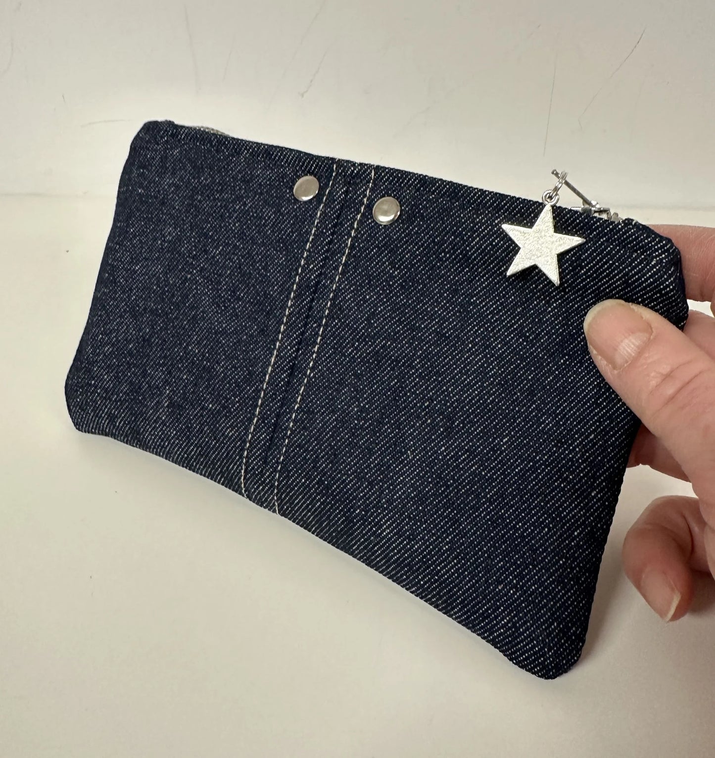 Le porte-monnaie en denim brut, tenu en main.