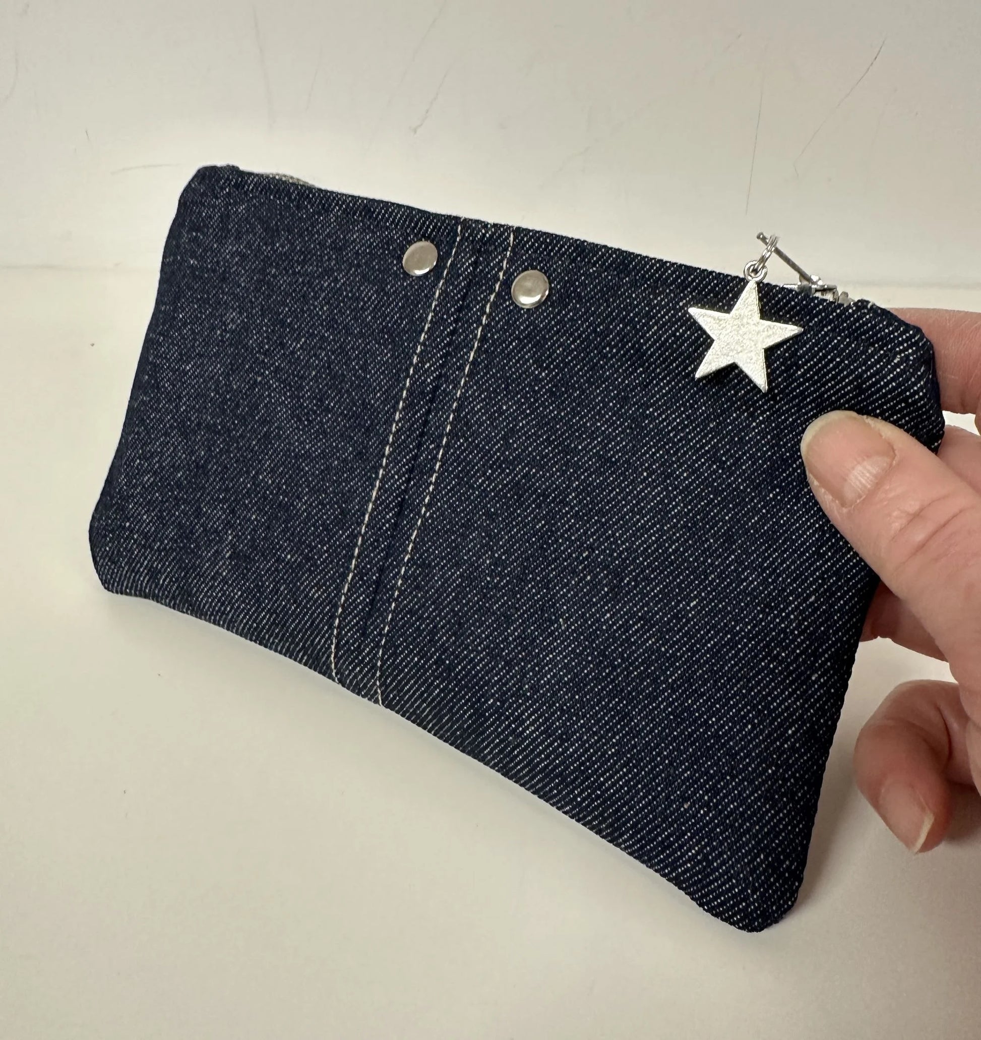 Le porte-monnaie en denim brut, tenu en main.
