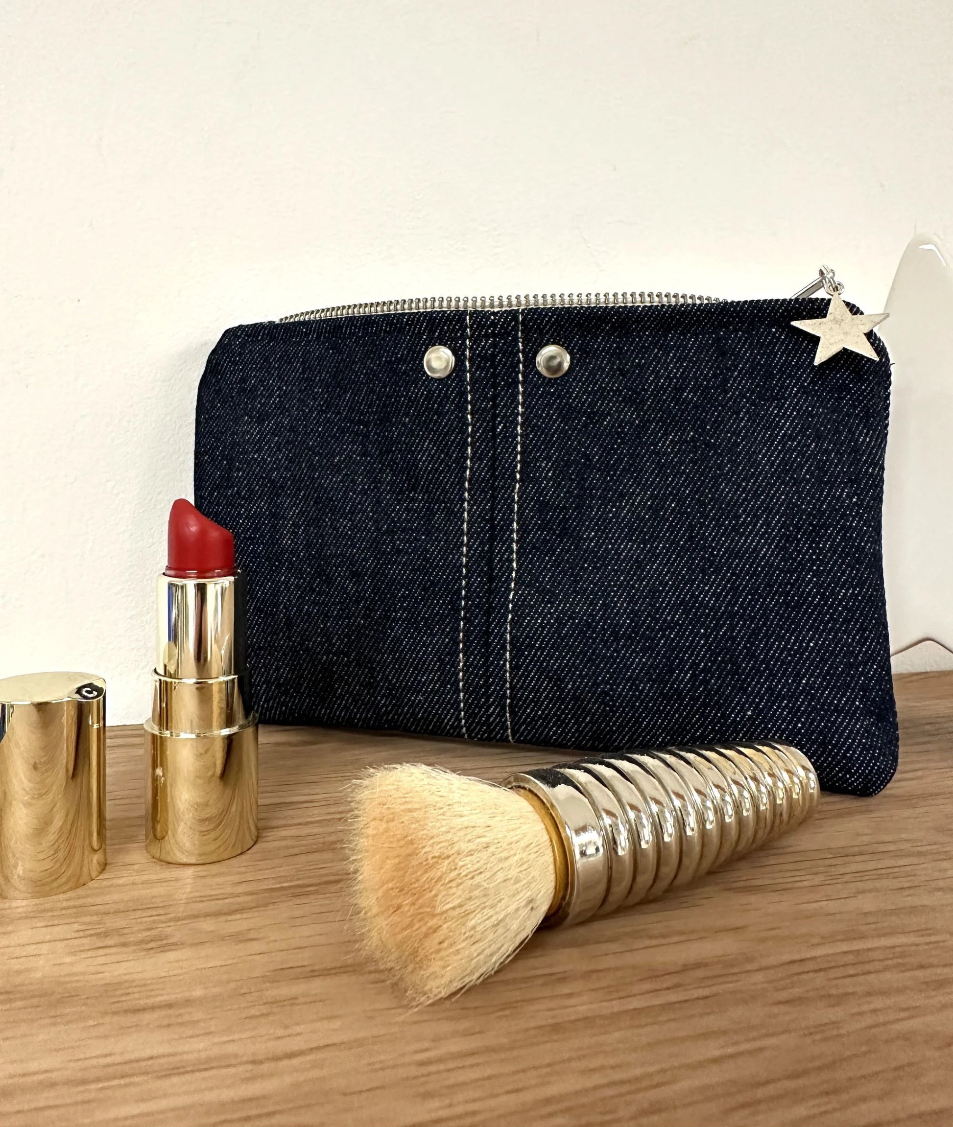 Le porte-monnaie en denim brut, avec ses surpiqures et rivets métalliques.