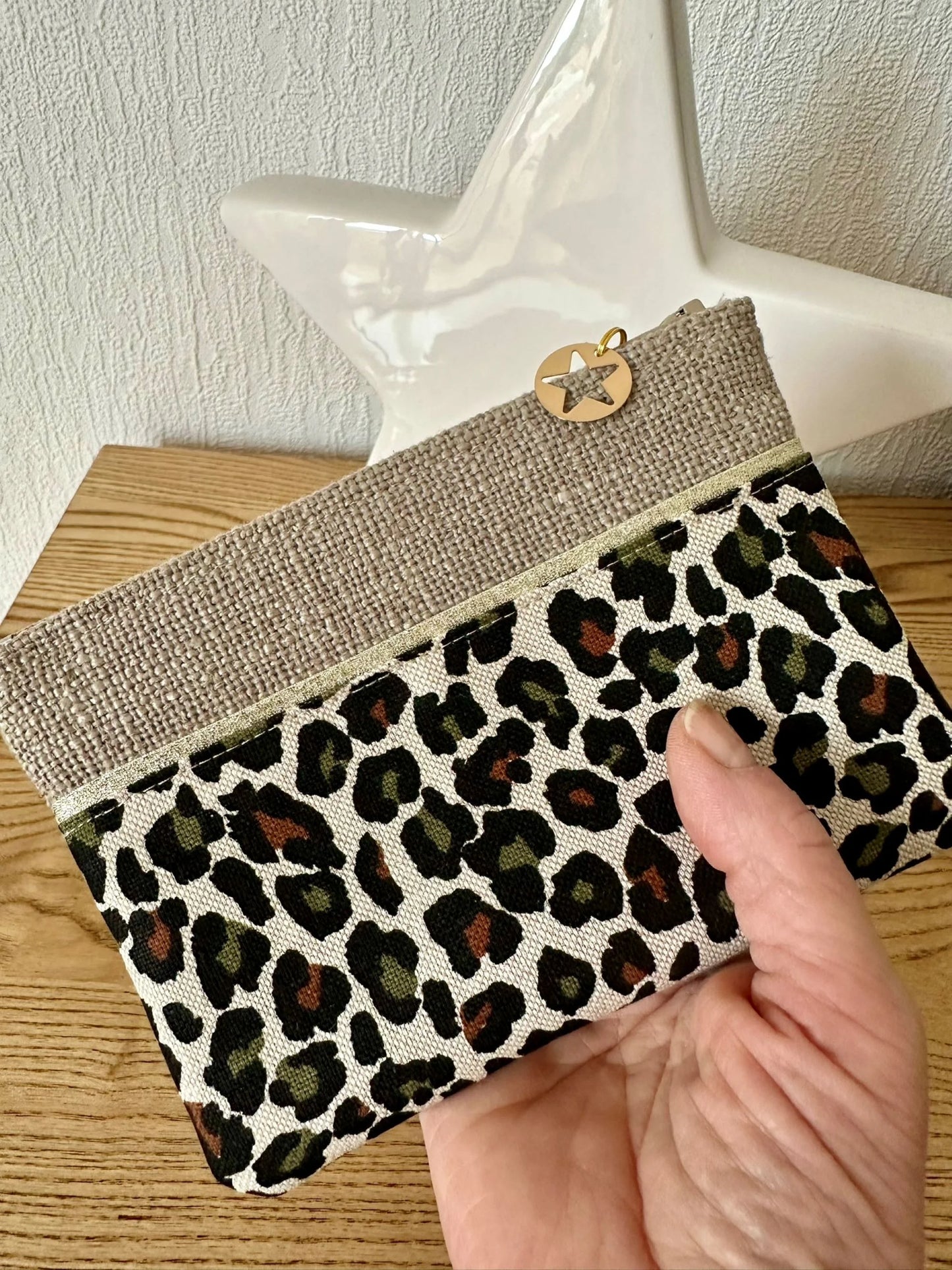 Le porte monnaie léopard en lin beige, tenu en main.
