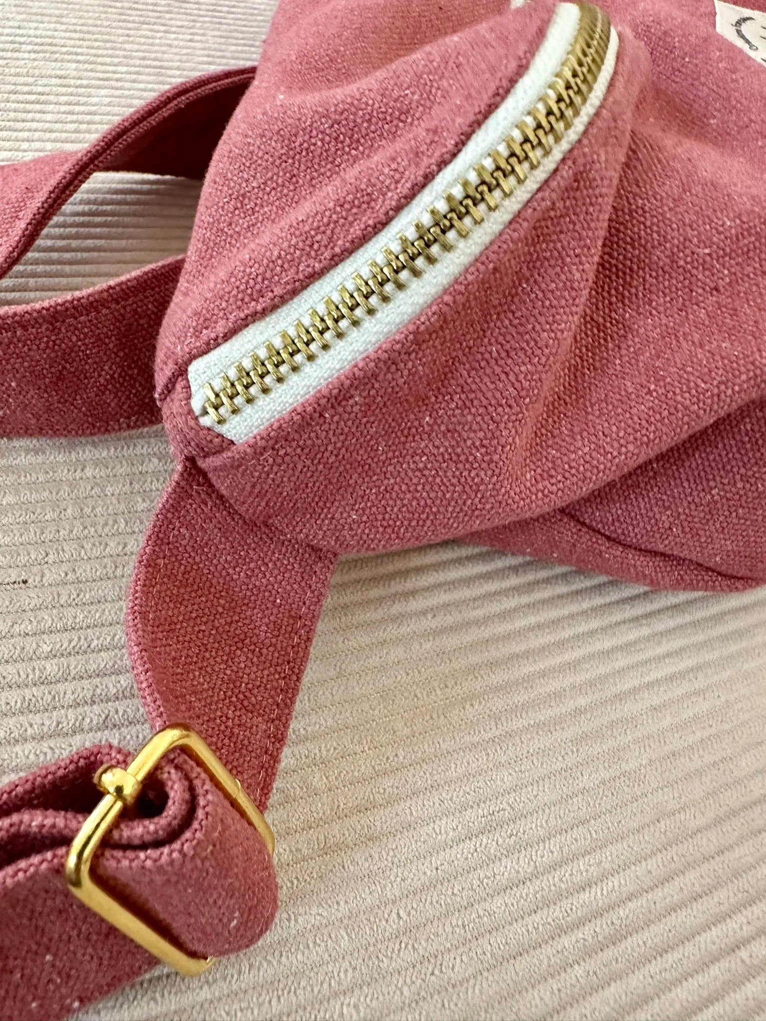 Vue détaillée de la fermeture métallique zippée du sac banane en toile framboise.