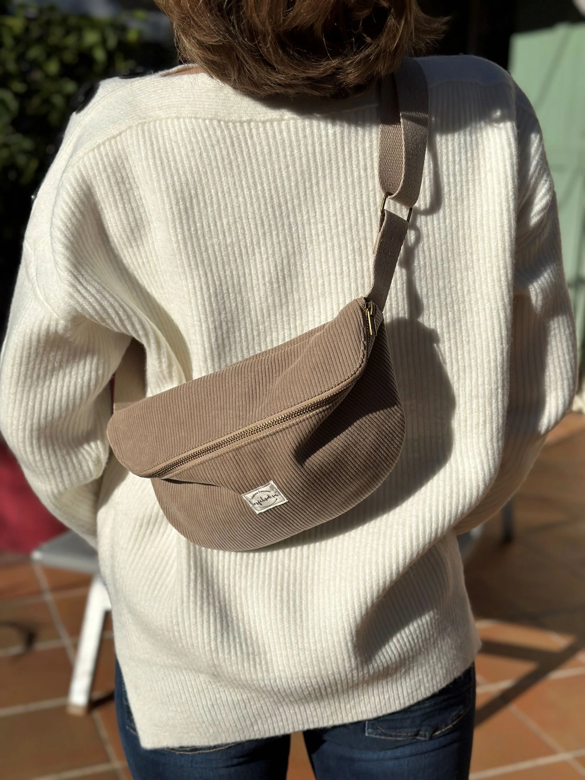 Le sac banane en velours côtelé beige, porté en travers.