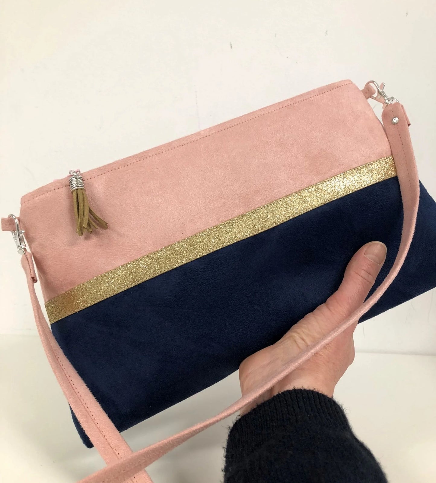 Le sac bandoulière Isa rose poudré et bleu marine à paillettes dorées, tenu en main.