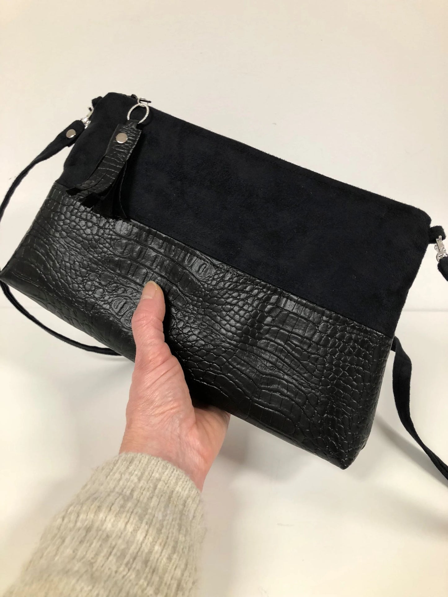 Le sac bandoulière Isa noir aspect reptile, tenu en main.