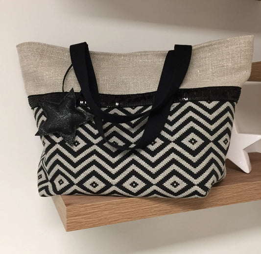 Le sac cabas Isa en lin et chevrons noirs à paillettes, posé et vue de face, avec son étoile amovible.