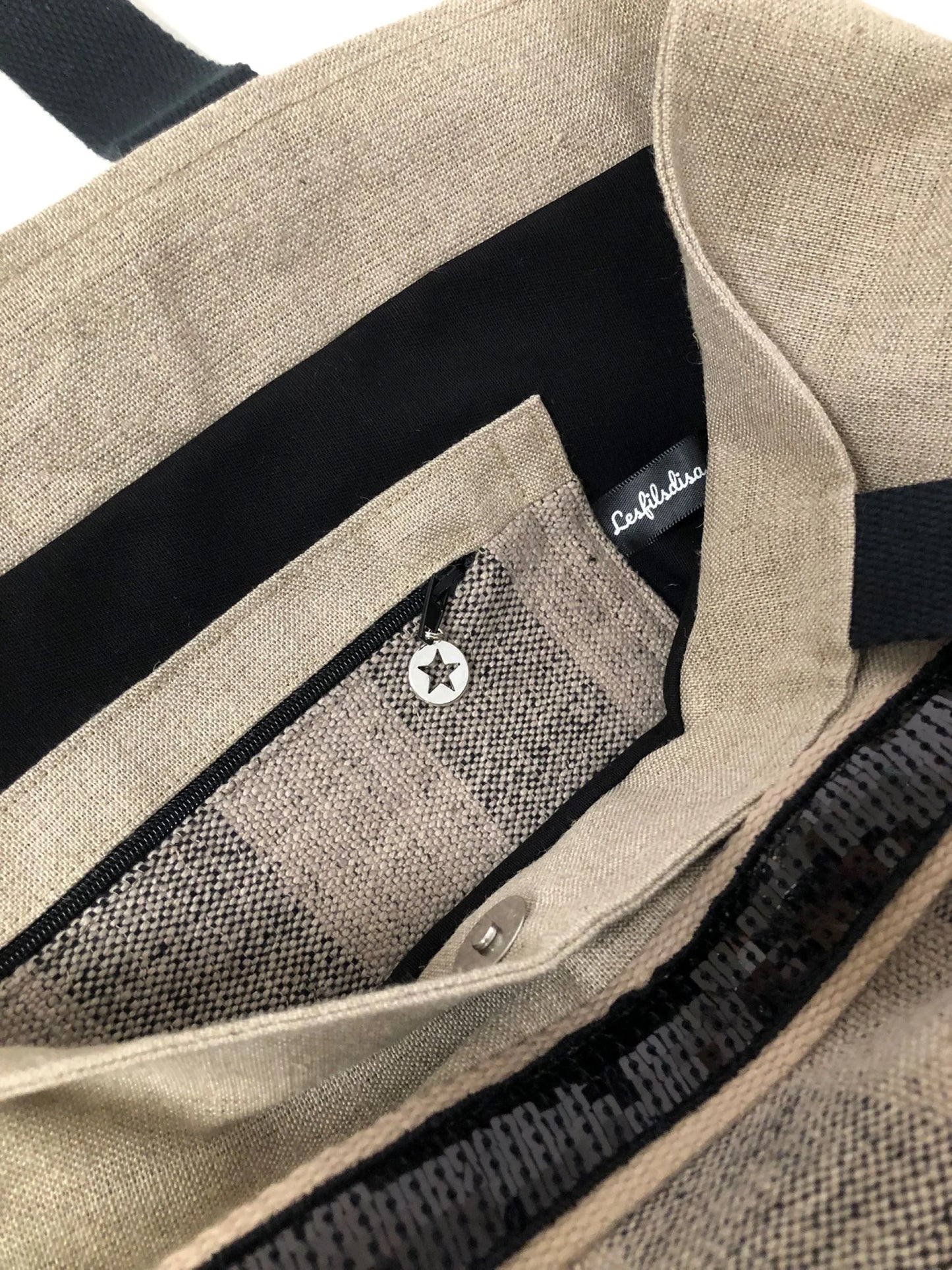 La poche intérieure zippée du sac cabas Isa en lin à larges rayures et paillettes noires.
