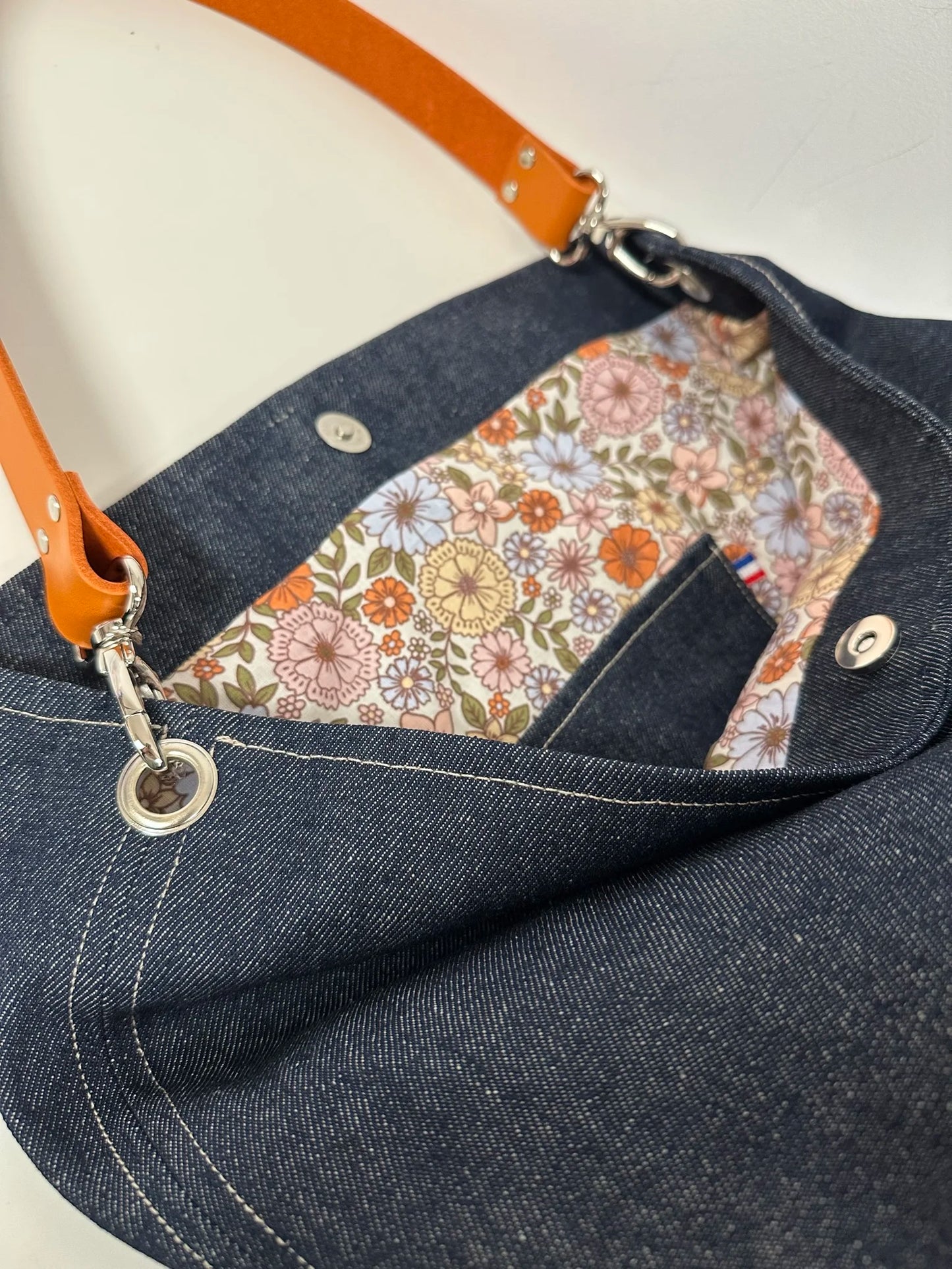 La poche plaquée intérieure du sac hobo en denim et son anse en cuir orange .